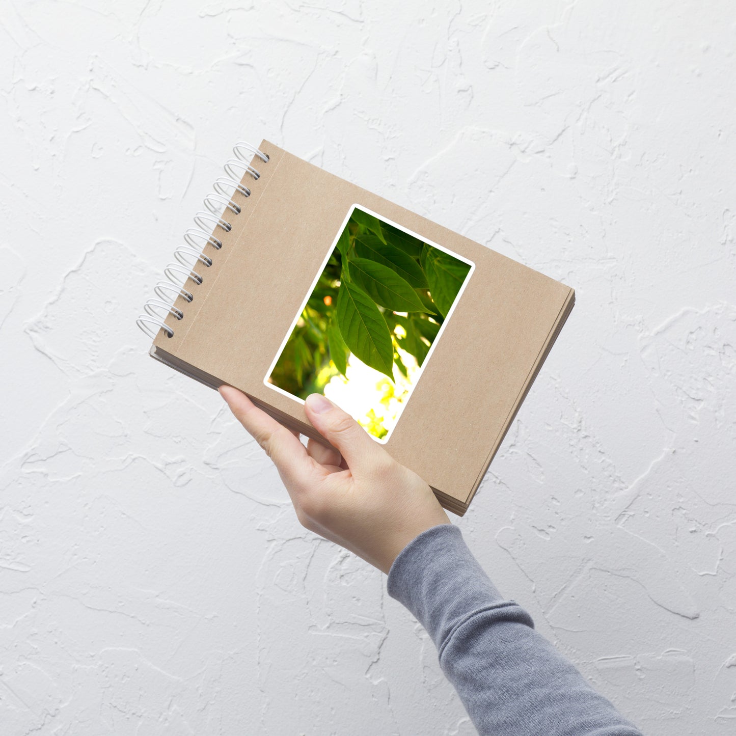 Lifestyle photo of a rectangular vinyl sticker with an image of backlit green leaves, placed on a small notepad.