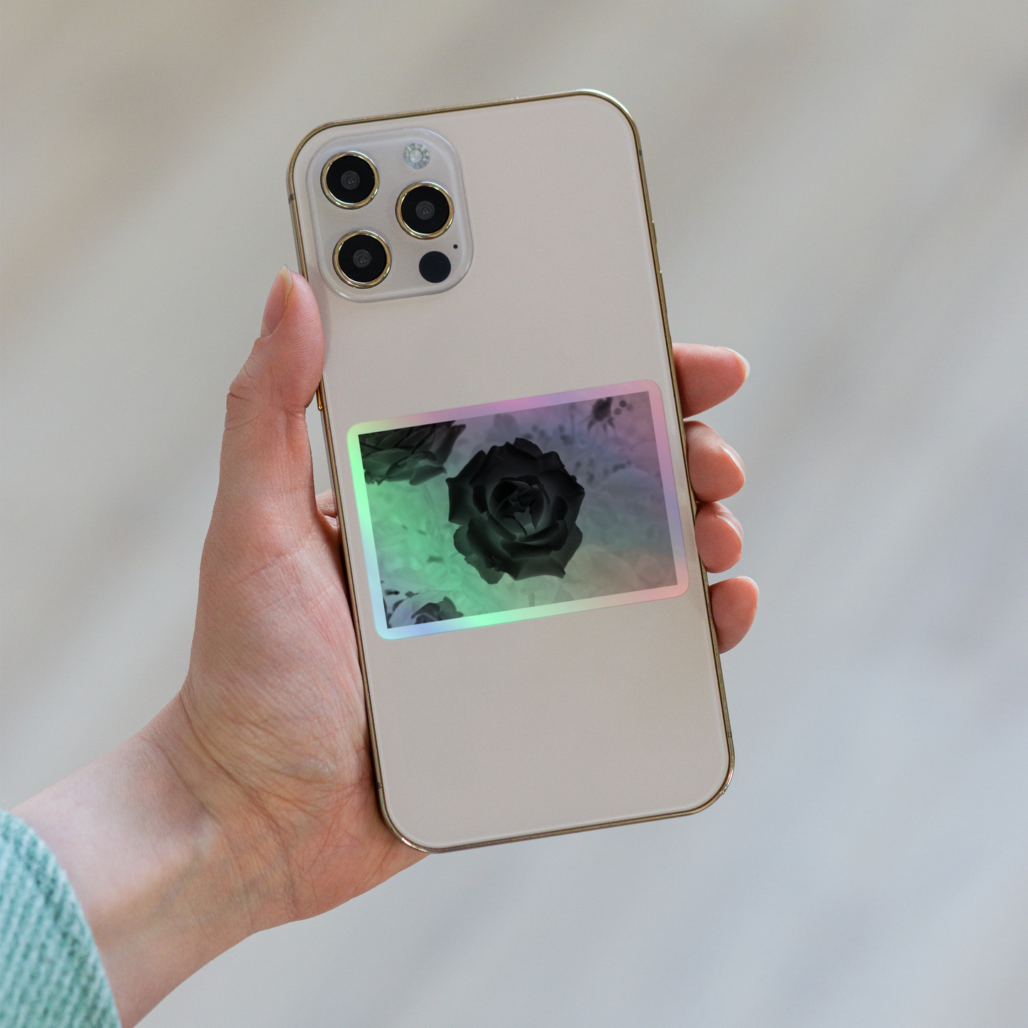 Lifestyle photo of a rectangular holographic sticker with an image of a black x-ray rose design, placed on the back of a phone.