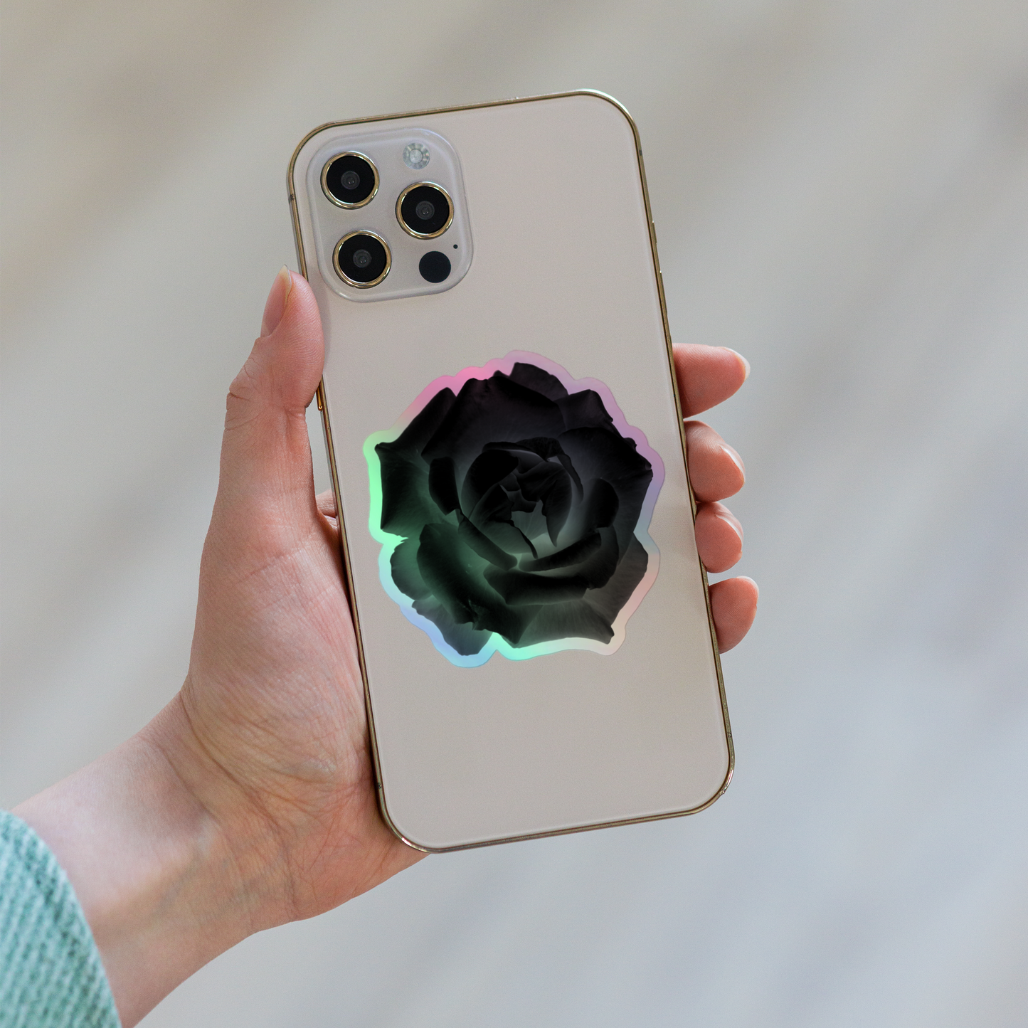 Lifestyle photo of a kiss-cut holographic sticker with an image of a black x-ray rose design, placed on the back of a phone.