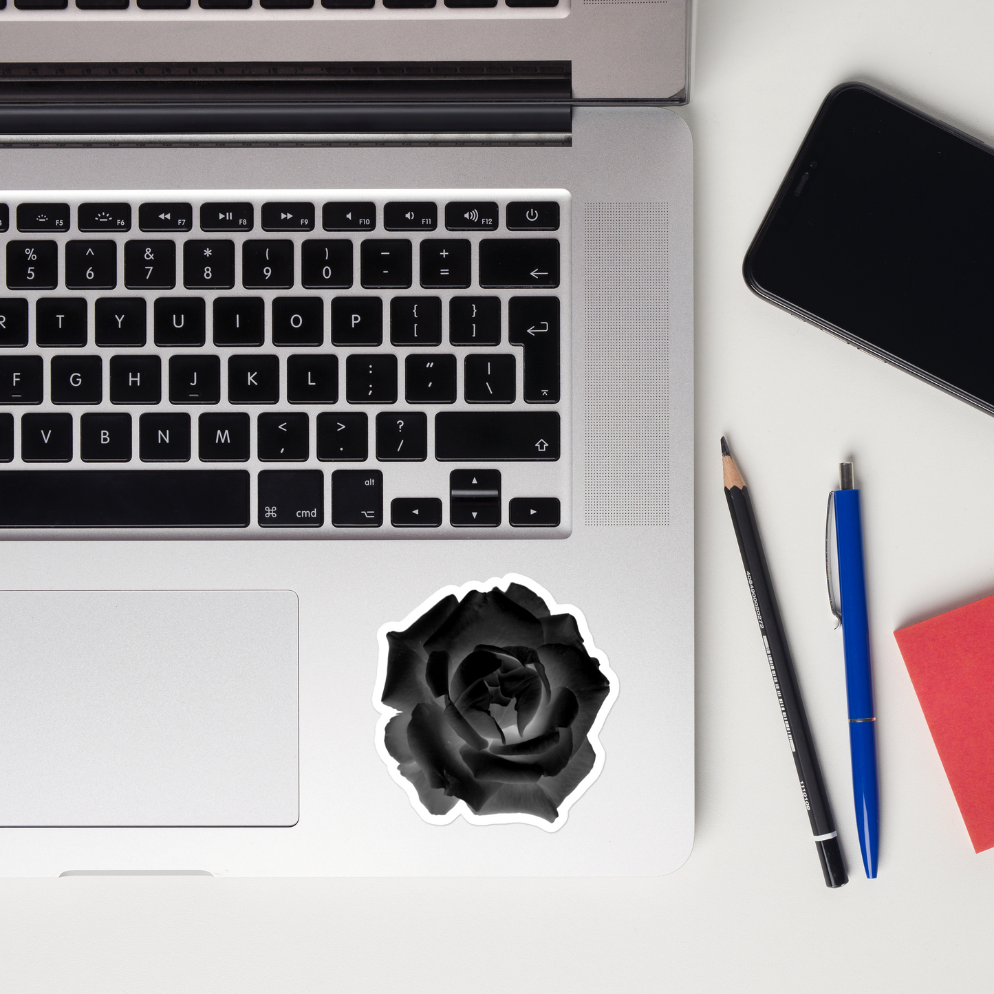 Lifestyle photo of a kiss-cut vinyl sticker with an image of a black x-ray rose design, placed on a laptop to the right of the mouse pad.