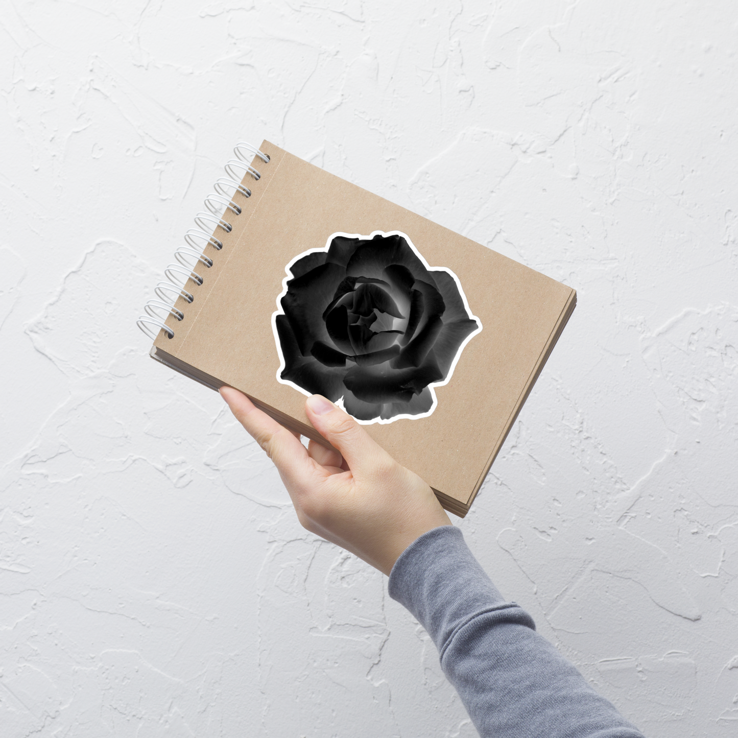 Lifestyle photo of a kiss-cut vinyl sticker with an image of a black x-ray rose design, placed on a small notepad.