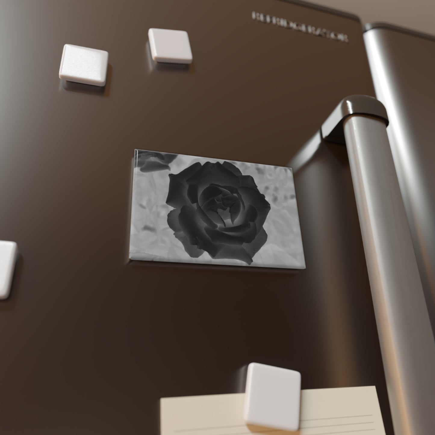 Lifestyle photo of a rectangular button magnet with an image of a black x-ray rose design, placed on a fridge.
