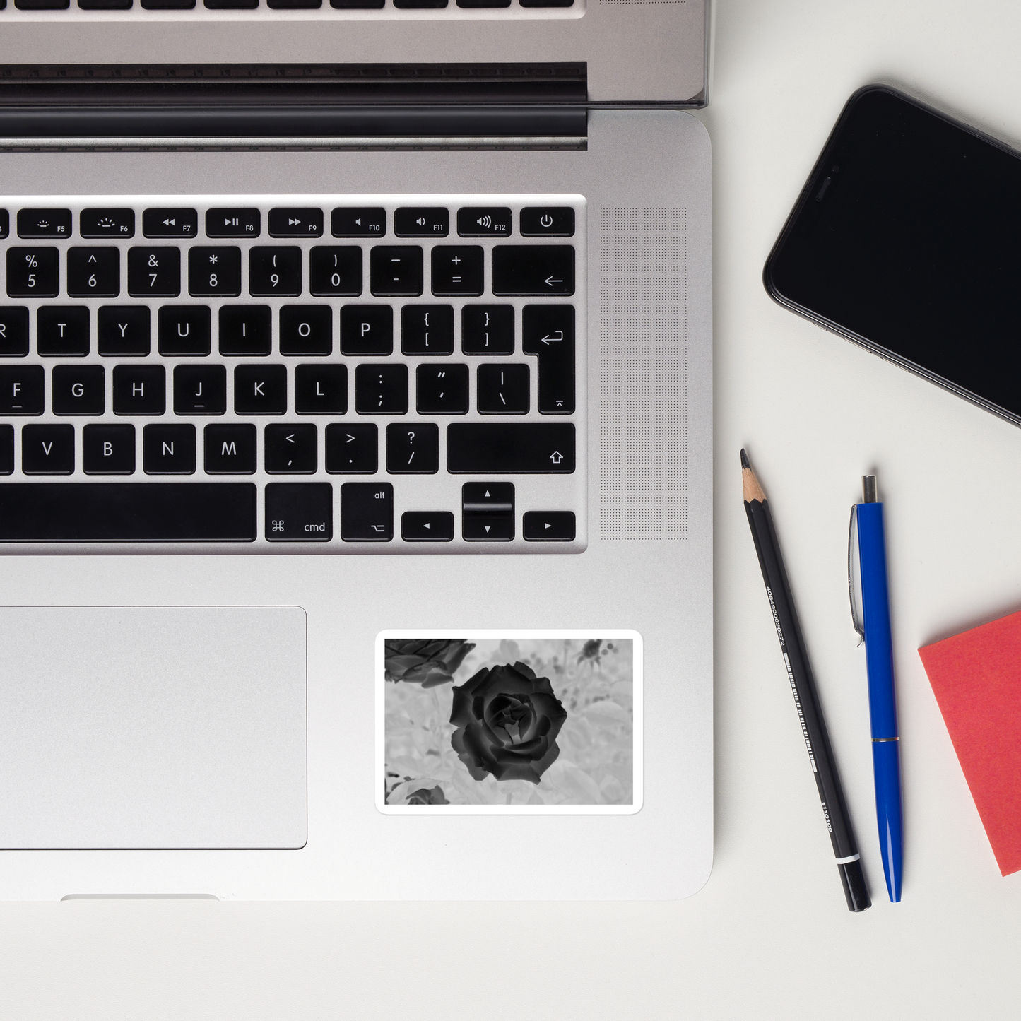 Lifestyle photo of a rectangular vinyl sticker with an image of a black x-ray rose design, placed on a laptop to the right of the mouse pad.