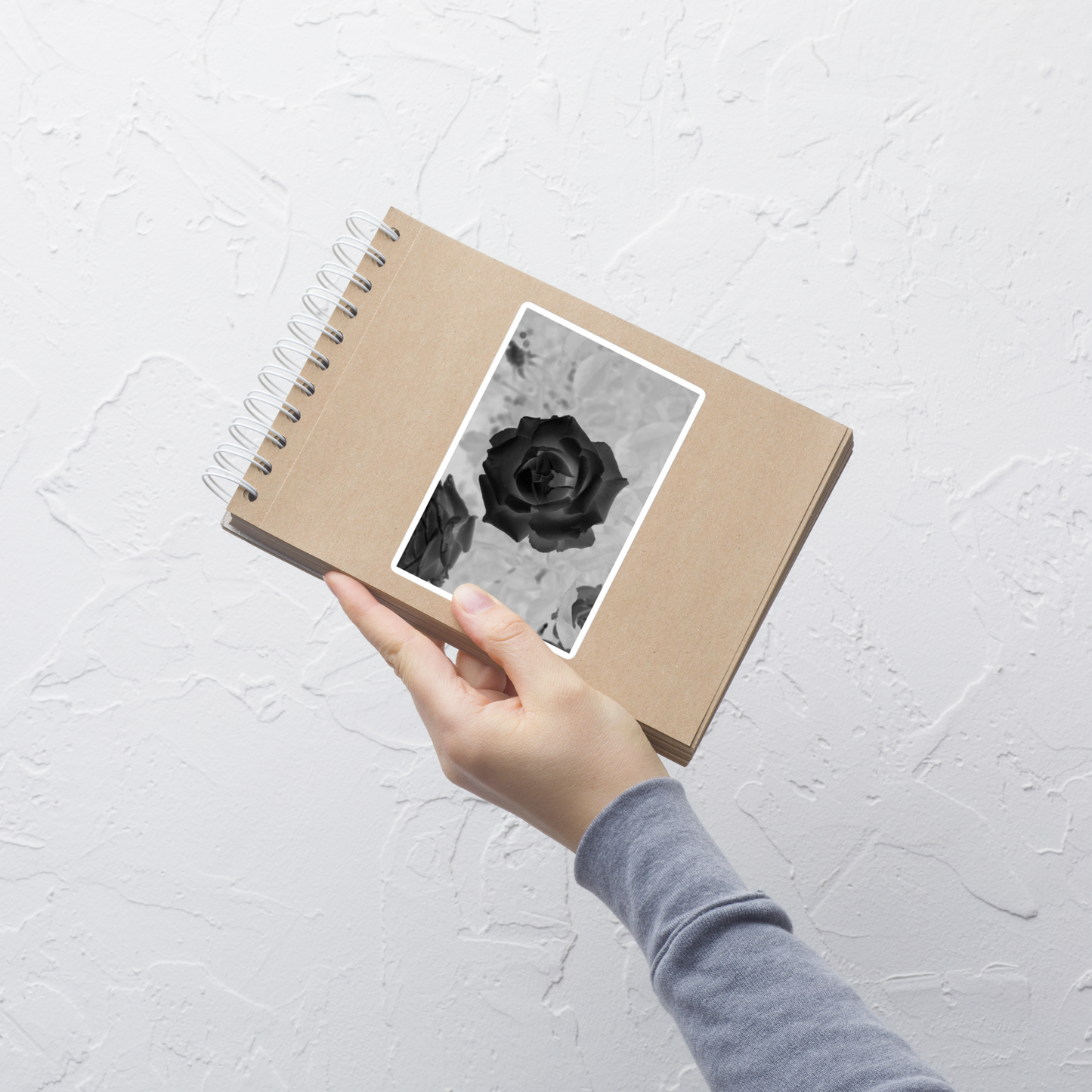 Lifestyle photo of a rectangular vinyl sticker with an image of a black x-ray rose design, placed on a small notepad.