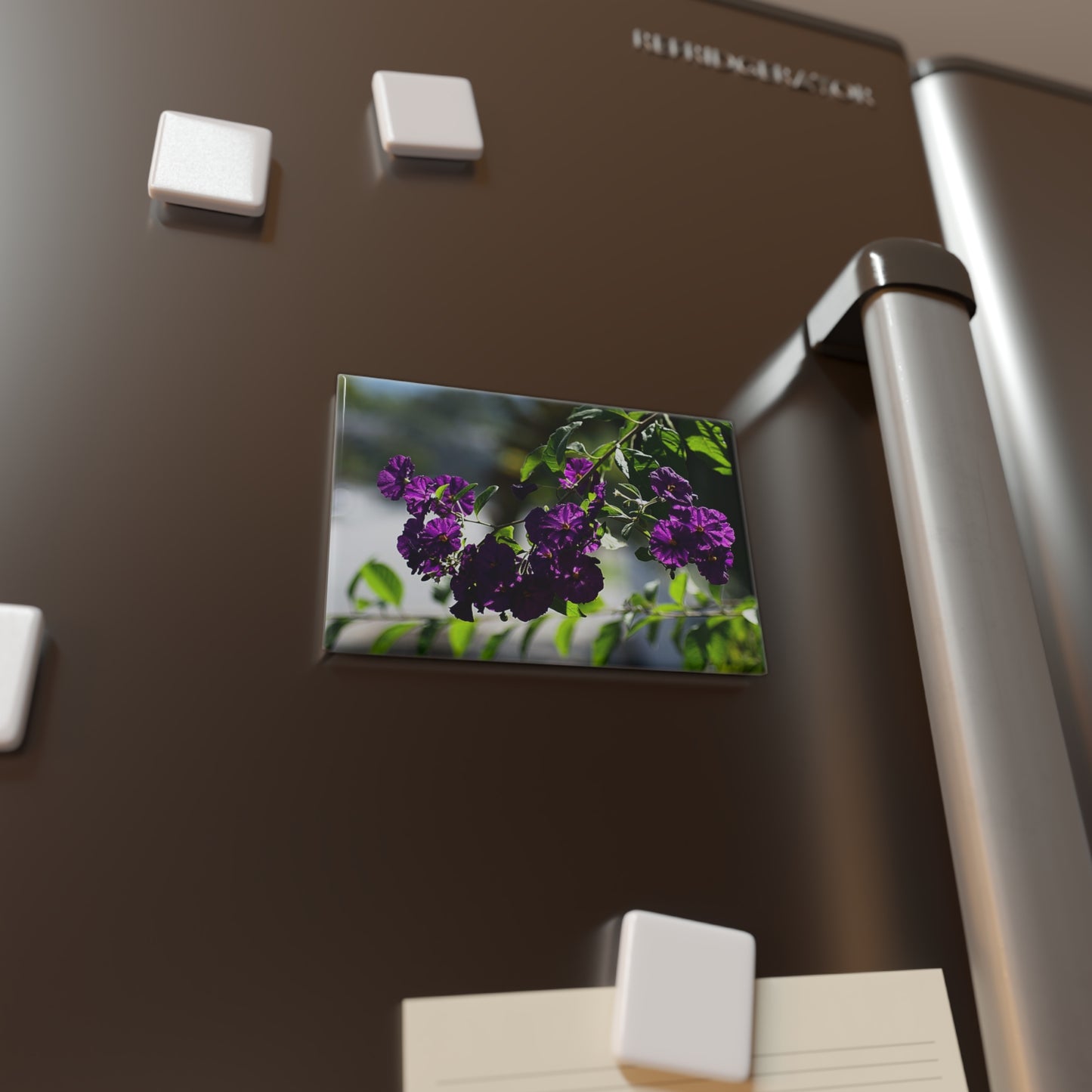 Lifestyle photo of a rectangular button magnet with an image of purple potato bush blooms, placed on a fridge.