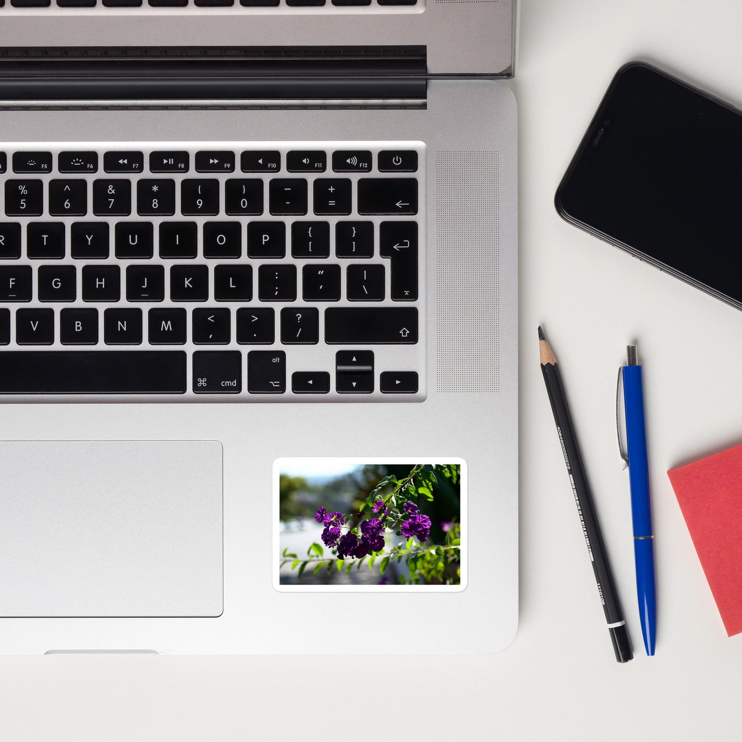 Lifestyle photo of a rectangular vinyl sticker with an image of purple flower blooms in a tree, placed on a laptop to the right of the mouse pad.