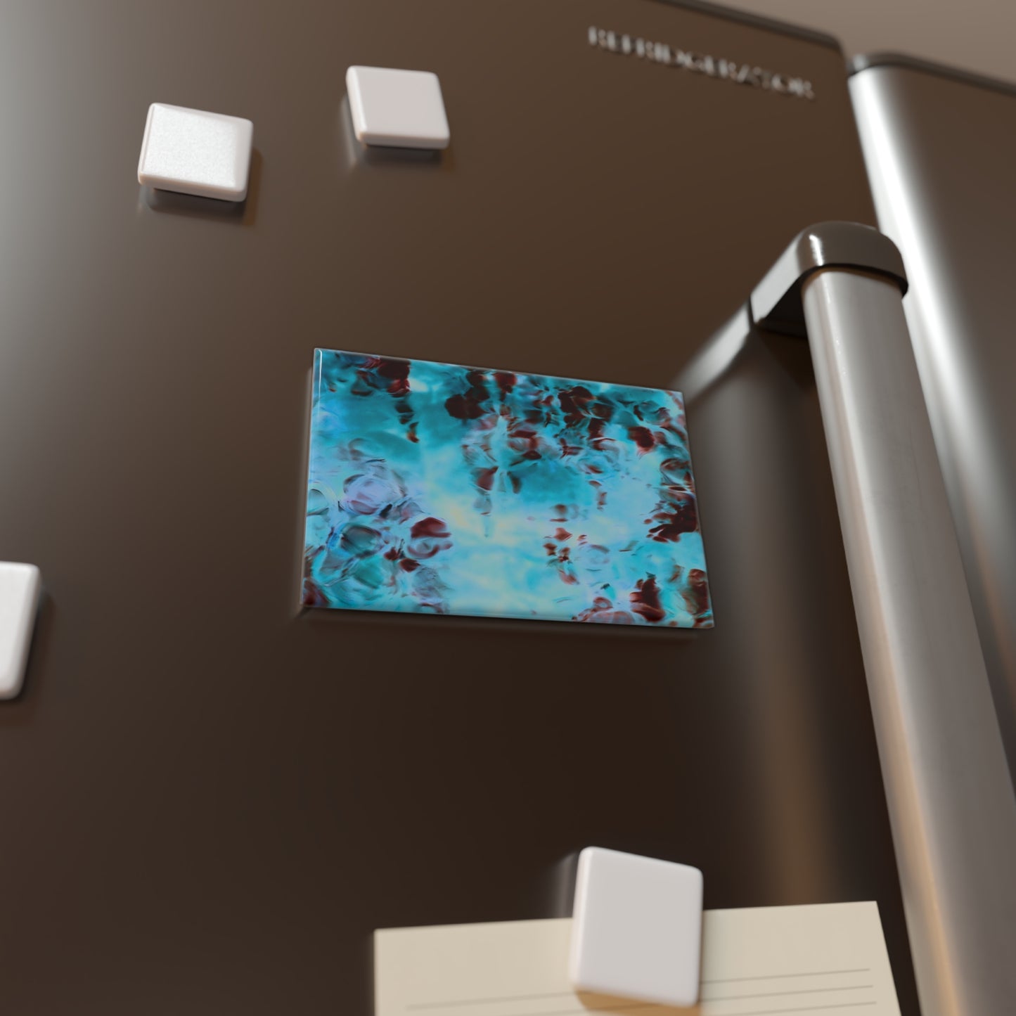 Lifestyle photo of a rectangular button magnet with an image of a vivid blue and red water reflection design, placed on a fridge.