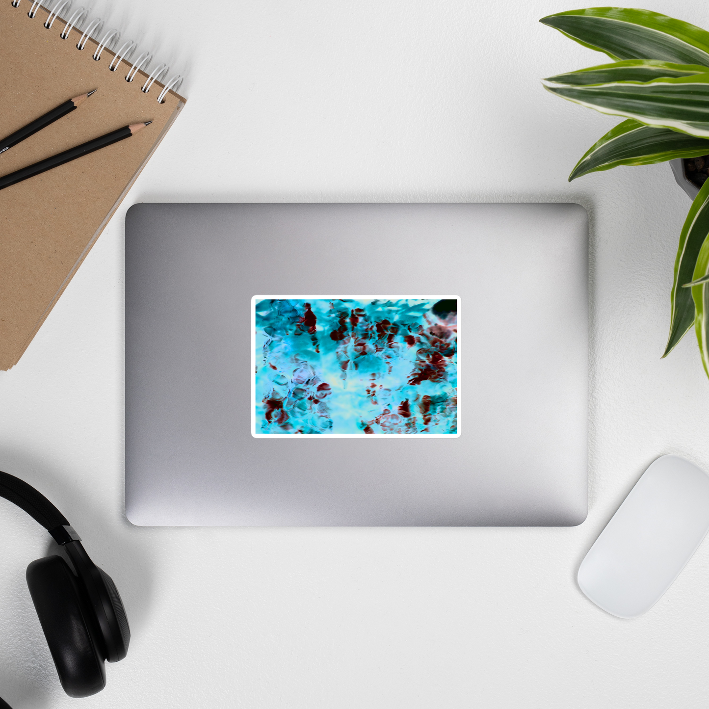 Lifestyle photo of a rectangular vinyl sticker with an image of a vivid blue and red water reflection design, placed on the outside of a laptop.