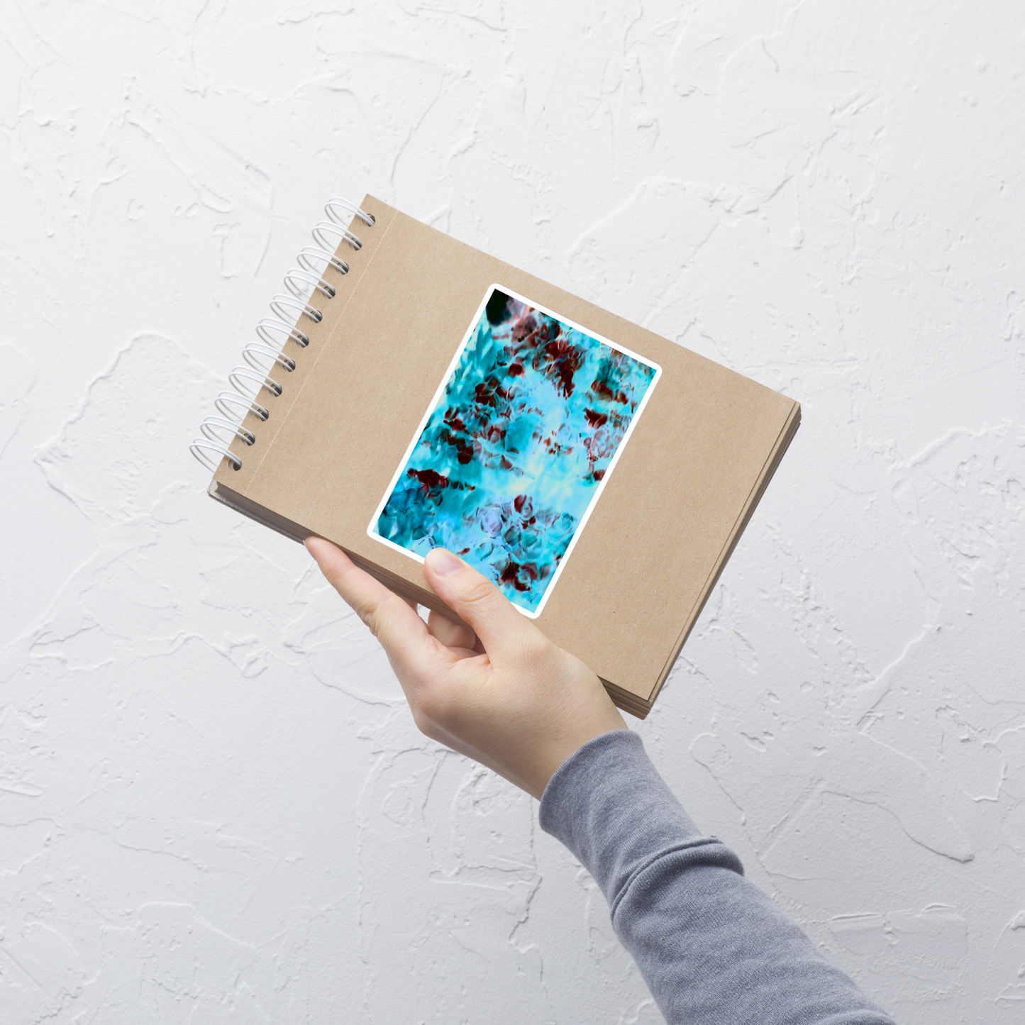 Lifestyle photo of a rectangular vinyl sticker with an image of a vivid blue and red water reflection design, placed on a small notepad.