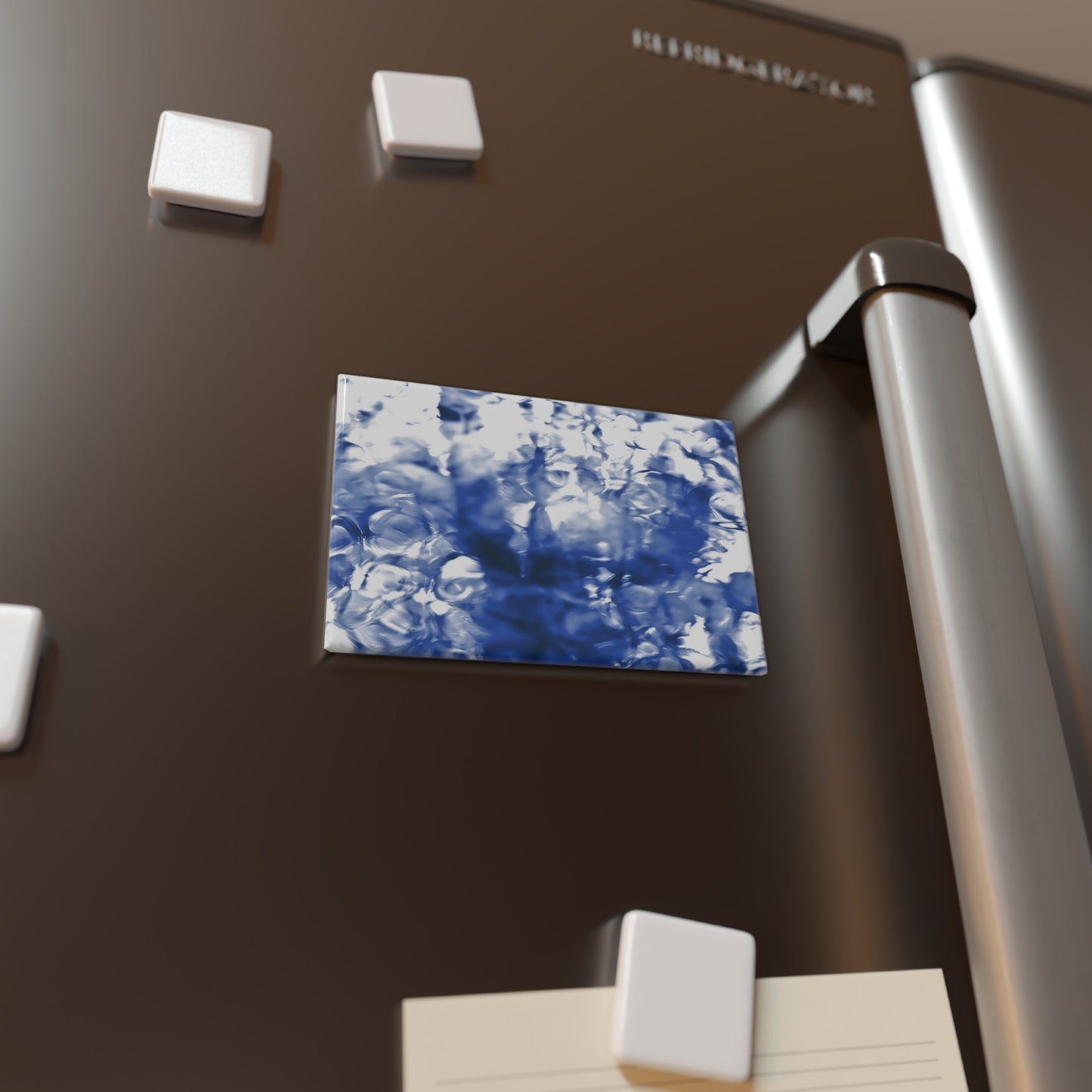 Lifestyle photo of a rectangular button magnet with an image of a vivid blue water reflection design, placed on a fridge.