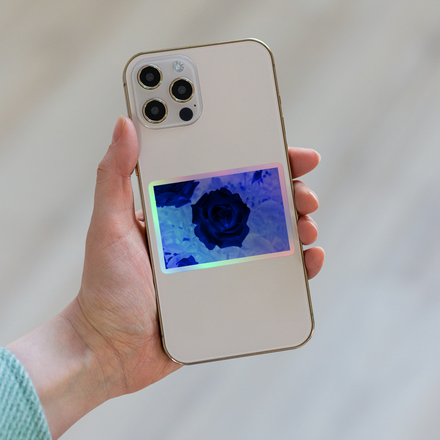 Lifestyle photo of a rectangular holographic sticker with an image of a blue x-ray rose design, placed on the back of a phone.