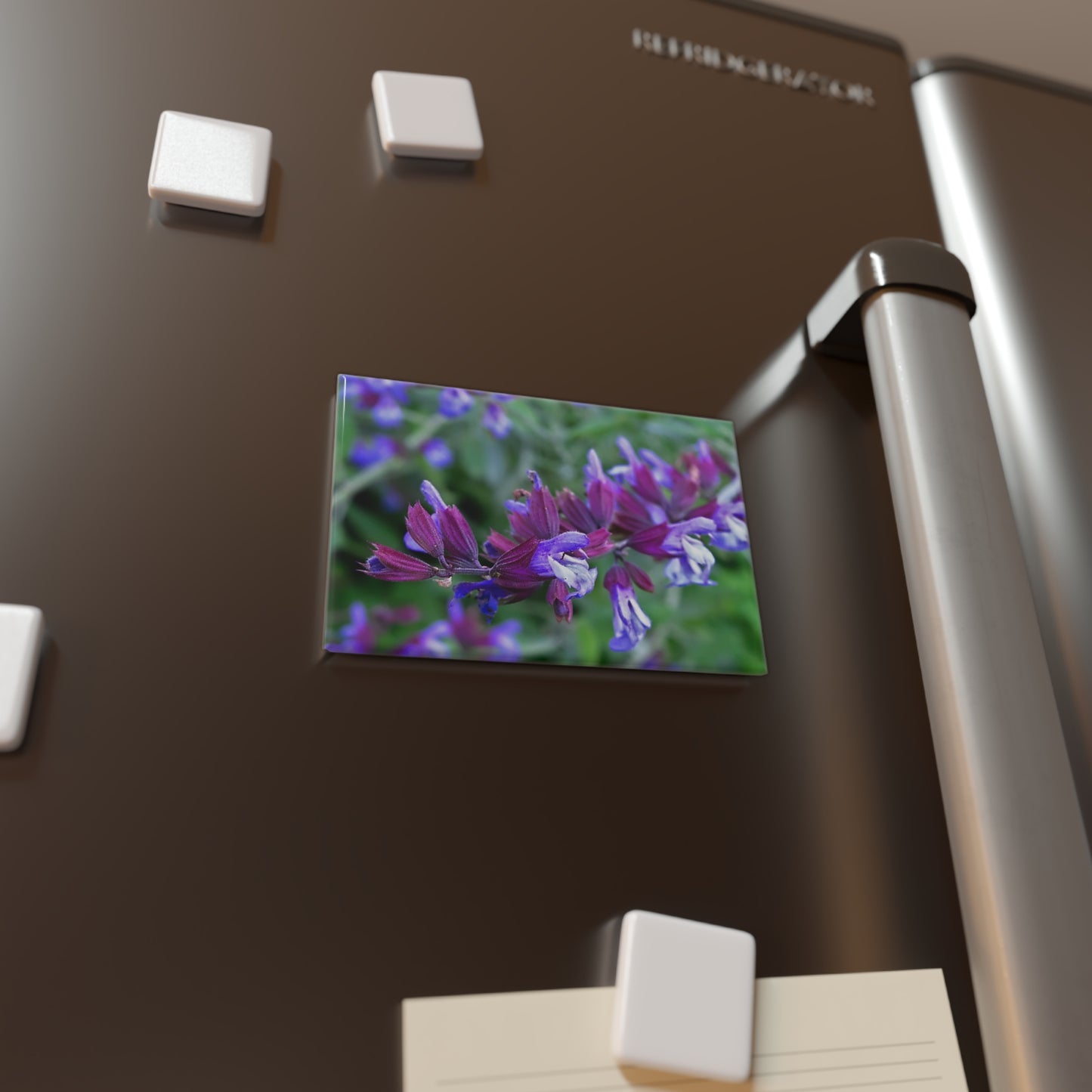 Lifestyle photo of a rectangular button magnet with an image of bright purple garden sage flowers, placed on a fridge.