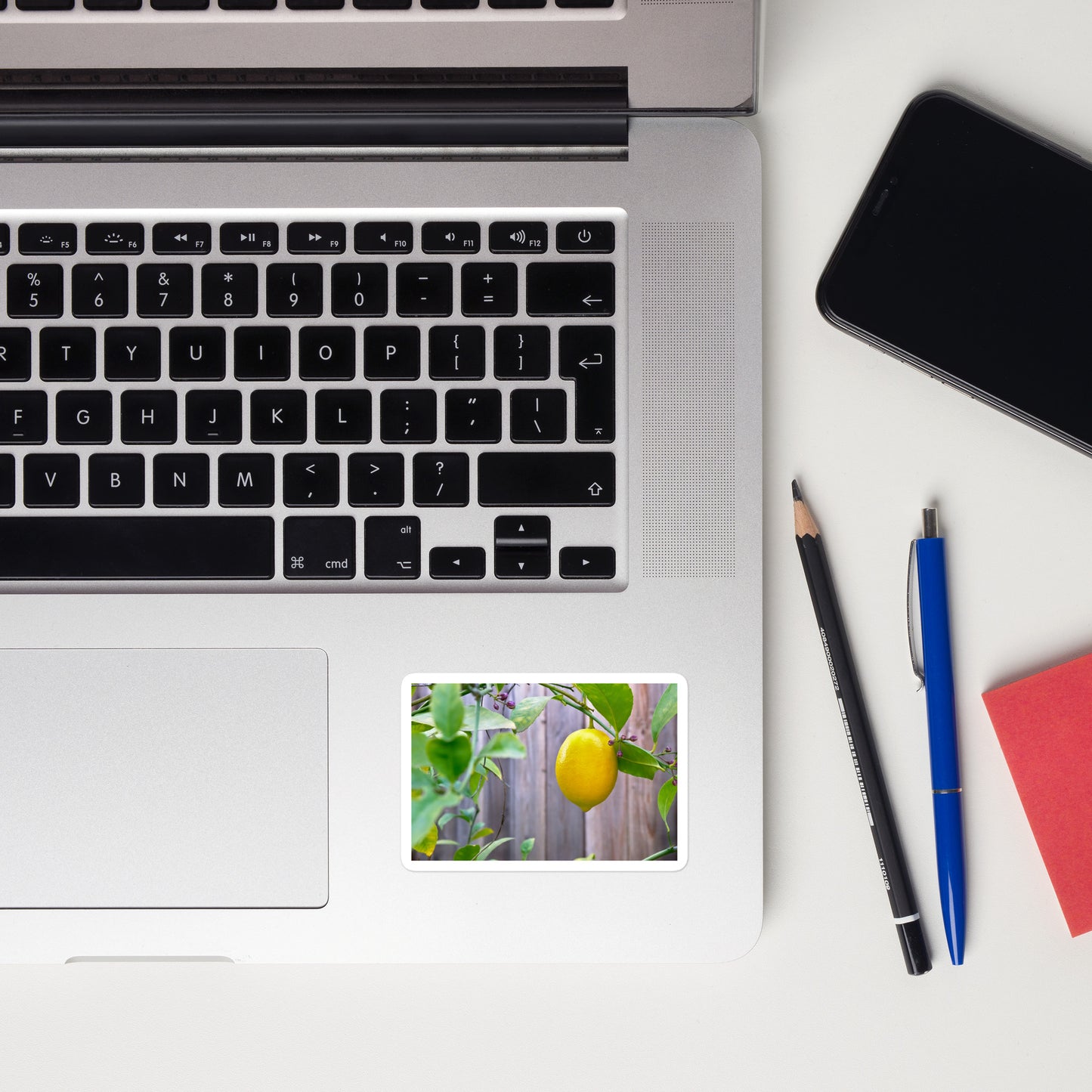 Lifestyle photo of a rectangular vinyl sticker with an image of a bright yellow lemon budding branches, placed on a laptop to the right of the mouse pad.