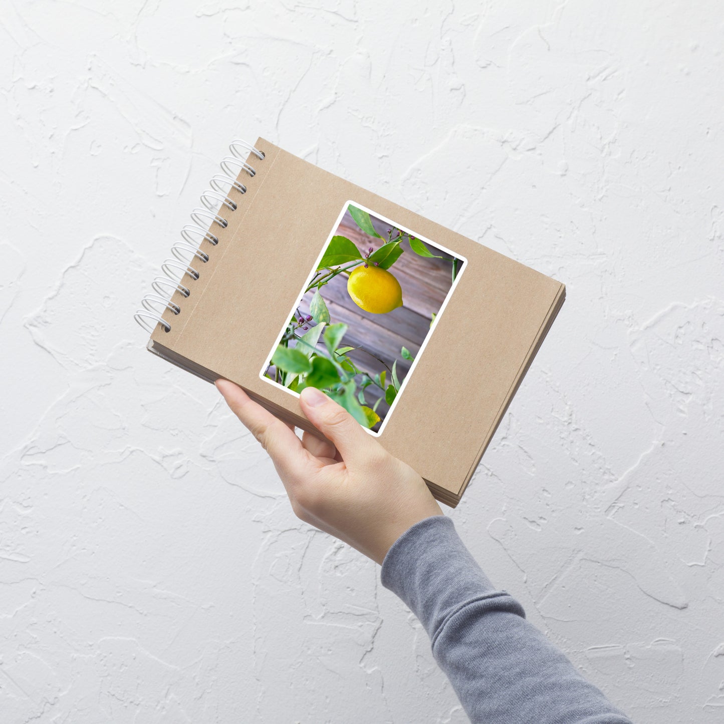 Lifestyle photo of a rectangular vinyl sticker with an image of a bright yellow lemon budding branches, placed on a small notepad.
