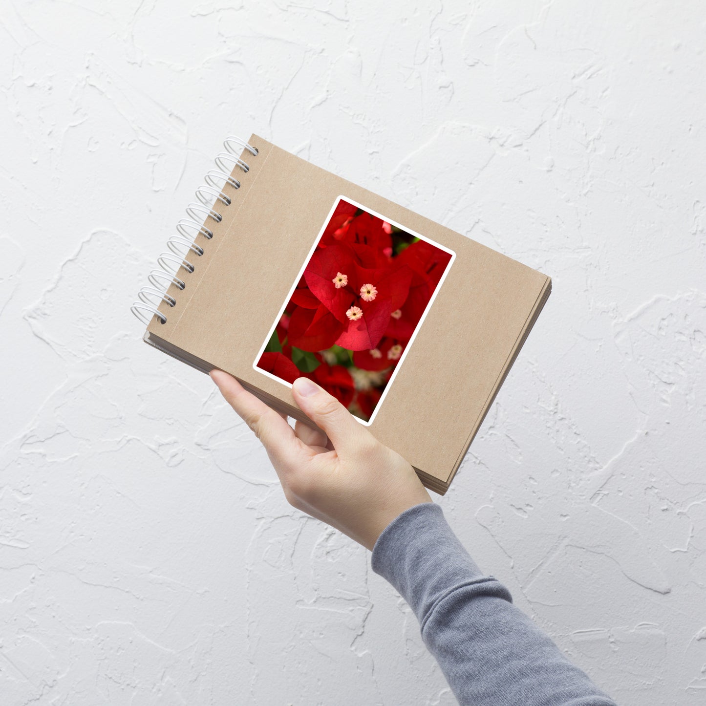 Lifestyle photo of a rectangular vinyl sticker with a close-up image of a red bougainvillea bloom, placed on a small notepad.