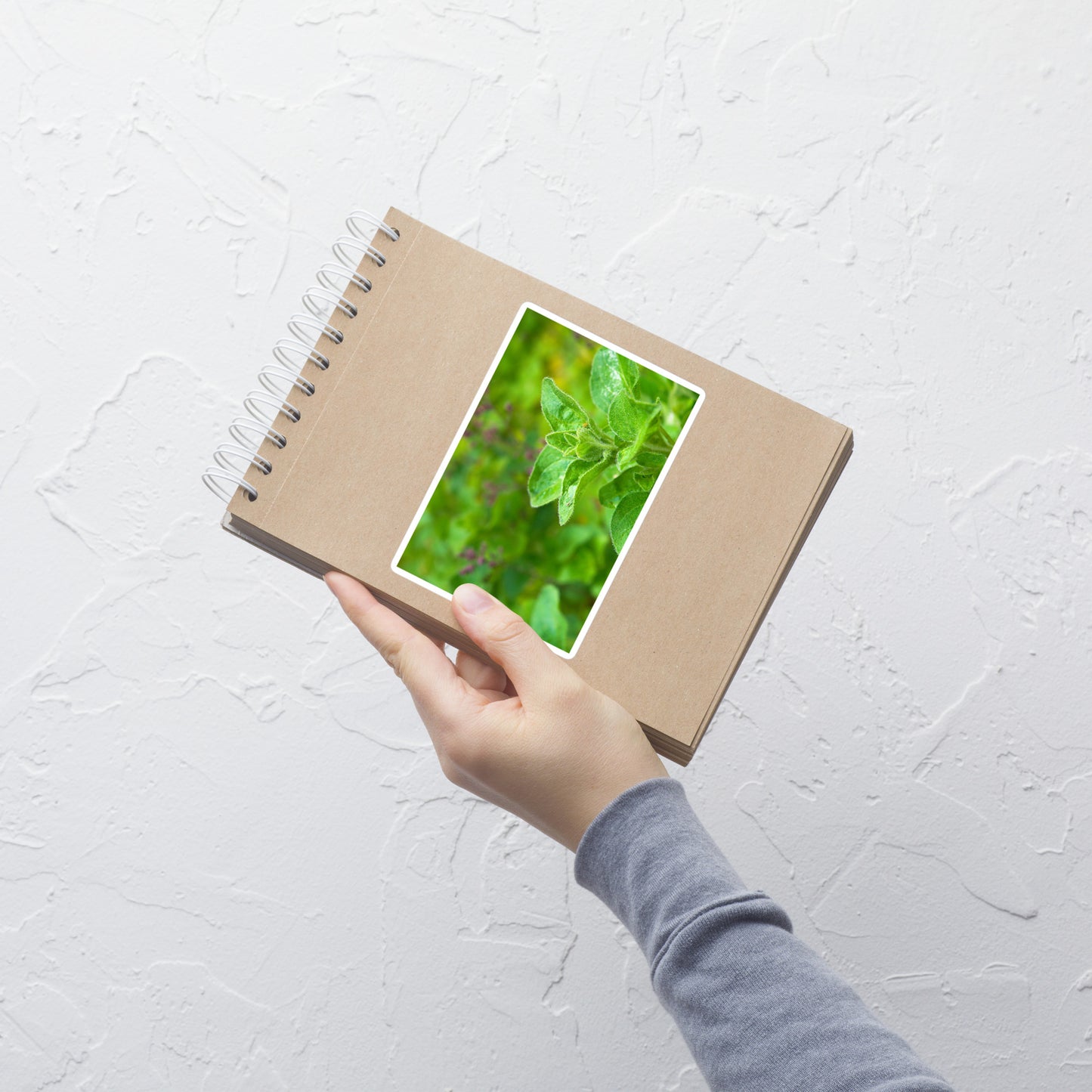 Lifestyle photo of a rectangular vinyl sticker with an image of an oregano sprig in an herb garden, placed on a small notepad.