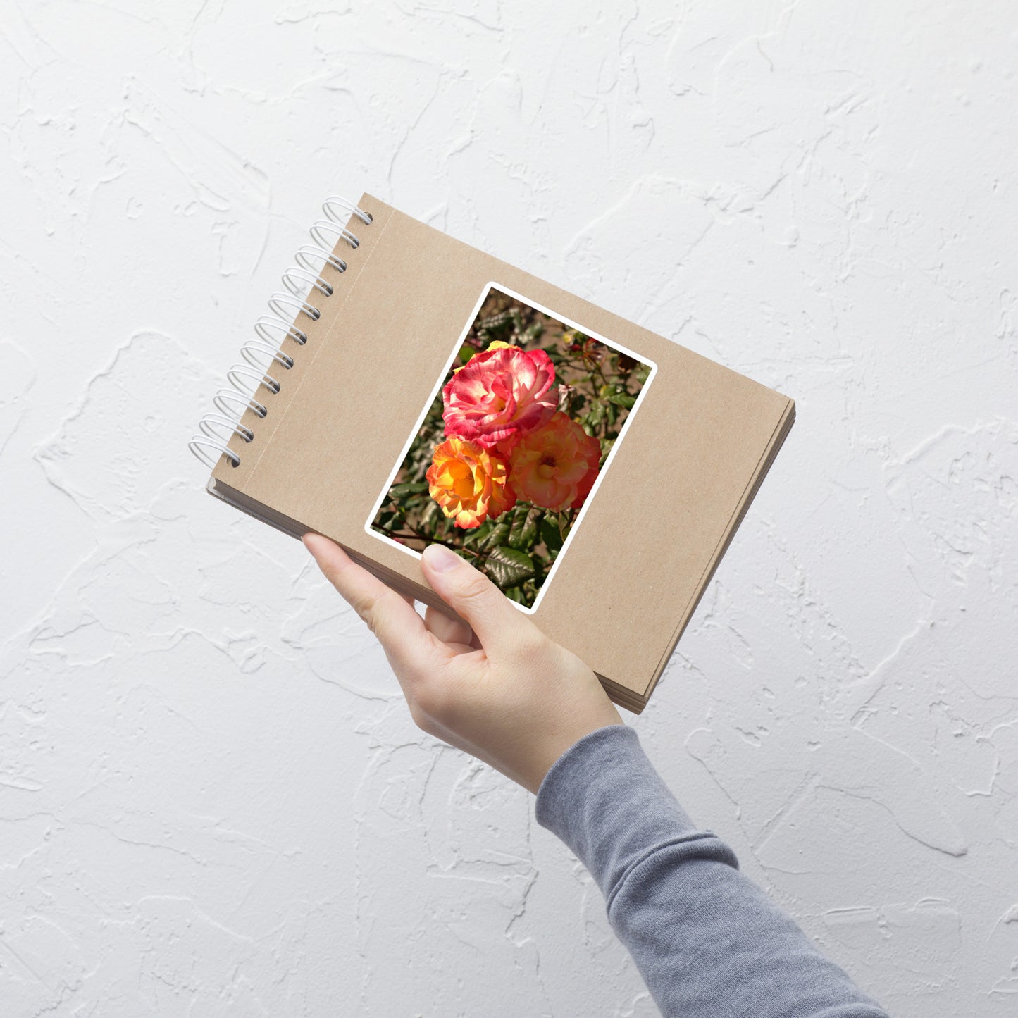 Lifestyle photo of a rectangular vinyl sticker with an image of three multi-colored pink and yellow roses, placed on a small notepad.