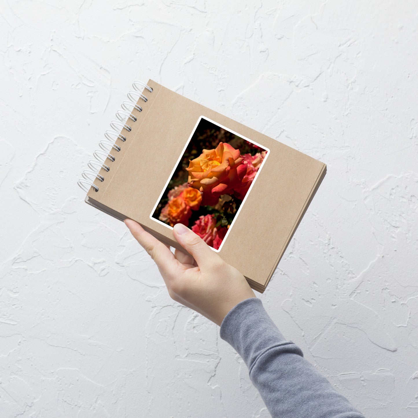 Lifestyle photo of a rectangular vinyl sticker with an image of pink, orange, and yellow roses, placed on a small notepad.