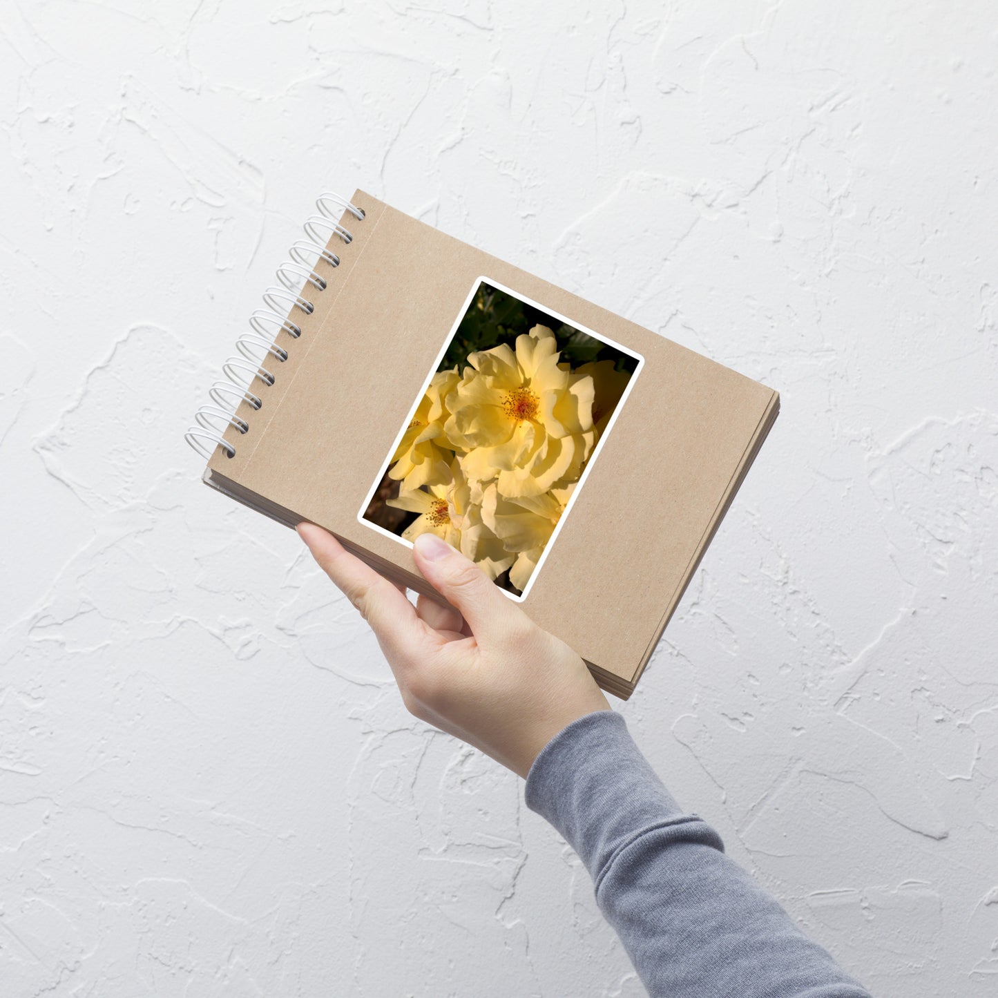 Lifestyle photo of a rectangular vinyl sticker with an image of pale yellow roses with visible stamen, placed on a small notepad.