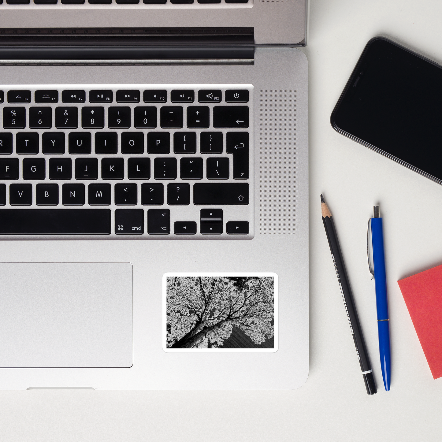 Lifestyle photo of a rectangular vinyl sticker with an image of an dark embossed tree design with lightning like features, placed on a laptop to the right of the mouse pad.