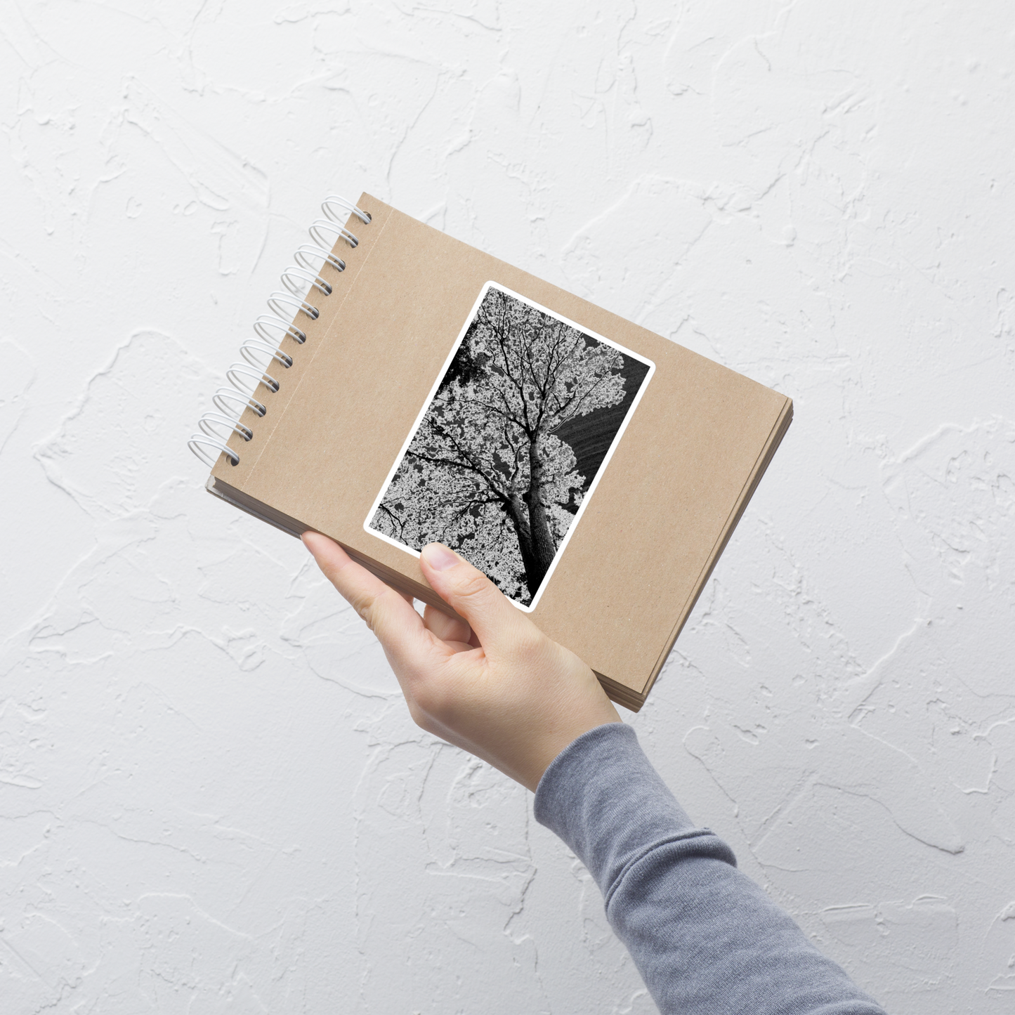 Lifestyle photo of a rectangular vinyl sticker with an image of an dark embossed tree design with lightning like features, placed on a small notepad.