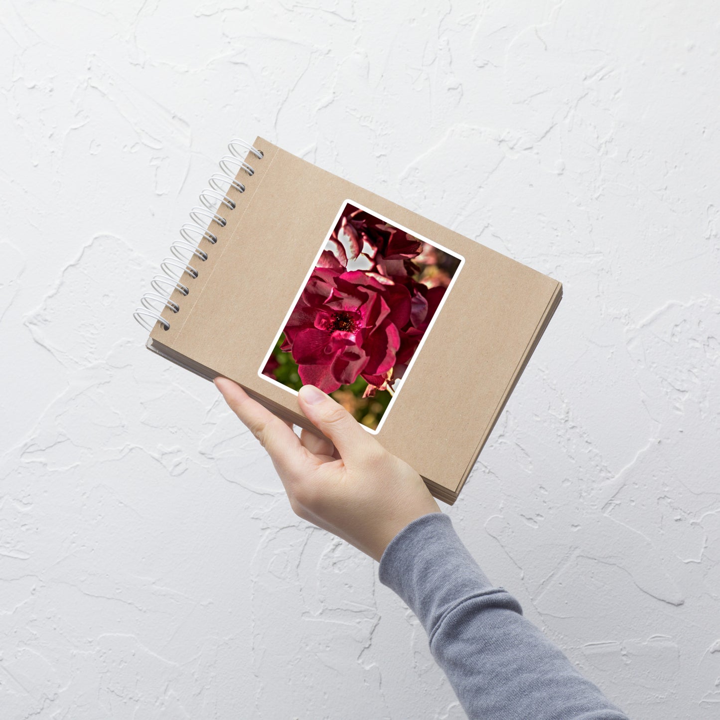 Lifestyle photo of a rectangular vinyl sticker with an image of a maroon colored rose bloom, placed on a small notepad.