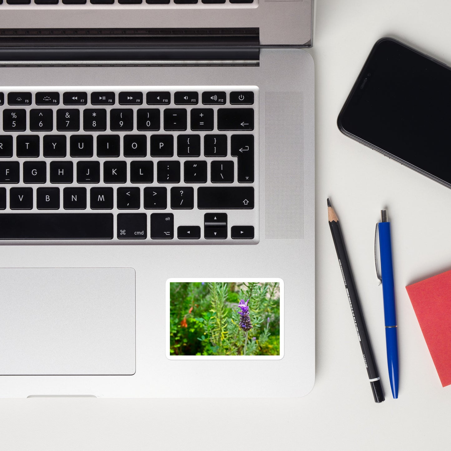 Lifestyle photo of a rectangular vinyl sticker with an image of a lavender bloom in an herb garden, placed on a laptop to the right of the mouse pad.