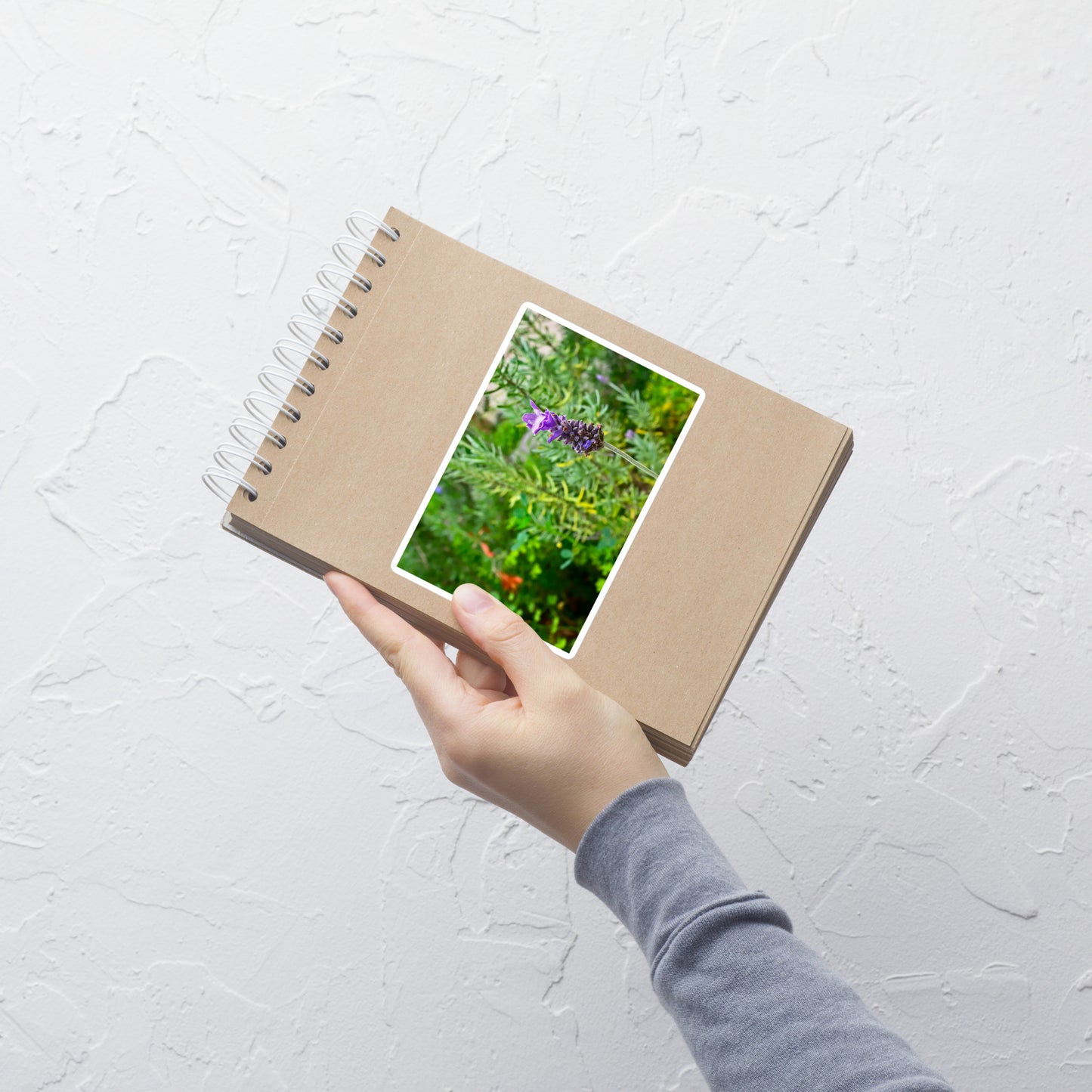 Lifestyle photo of a rectangular vinyl sticker with an image of a lavender bloom in an herb garden, placed on a small notepad.