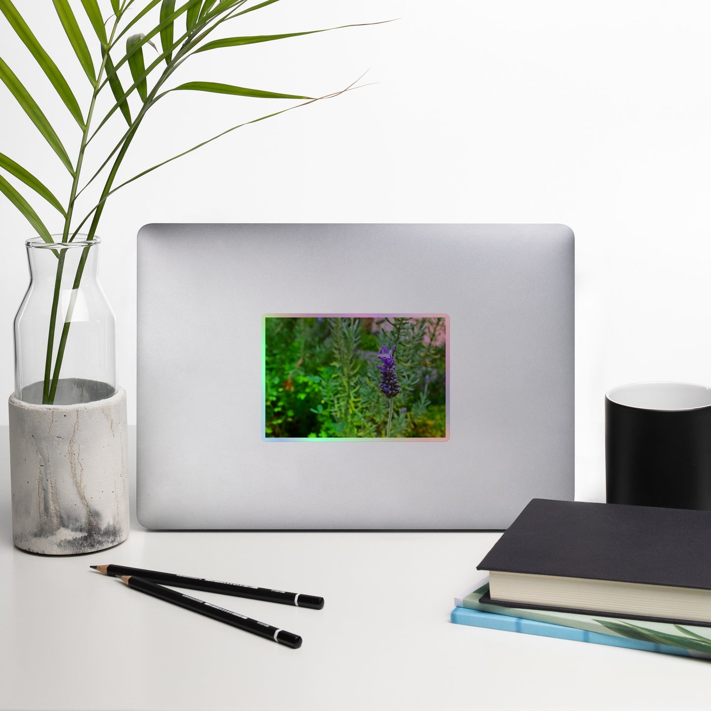 Lifestyle photo of a rectangular holographic sticker with an image of a purple lavender bloom in an herb garden, placed on a laptop with desk supplies nearby.