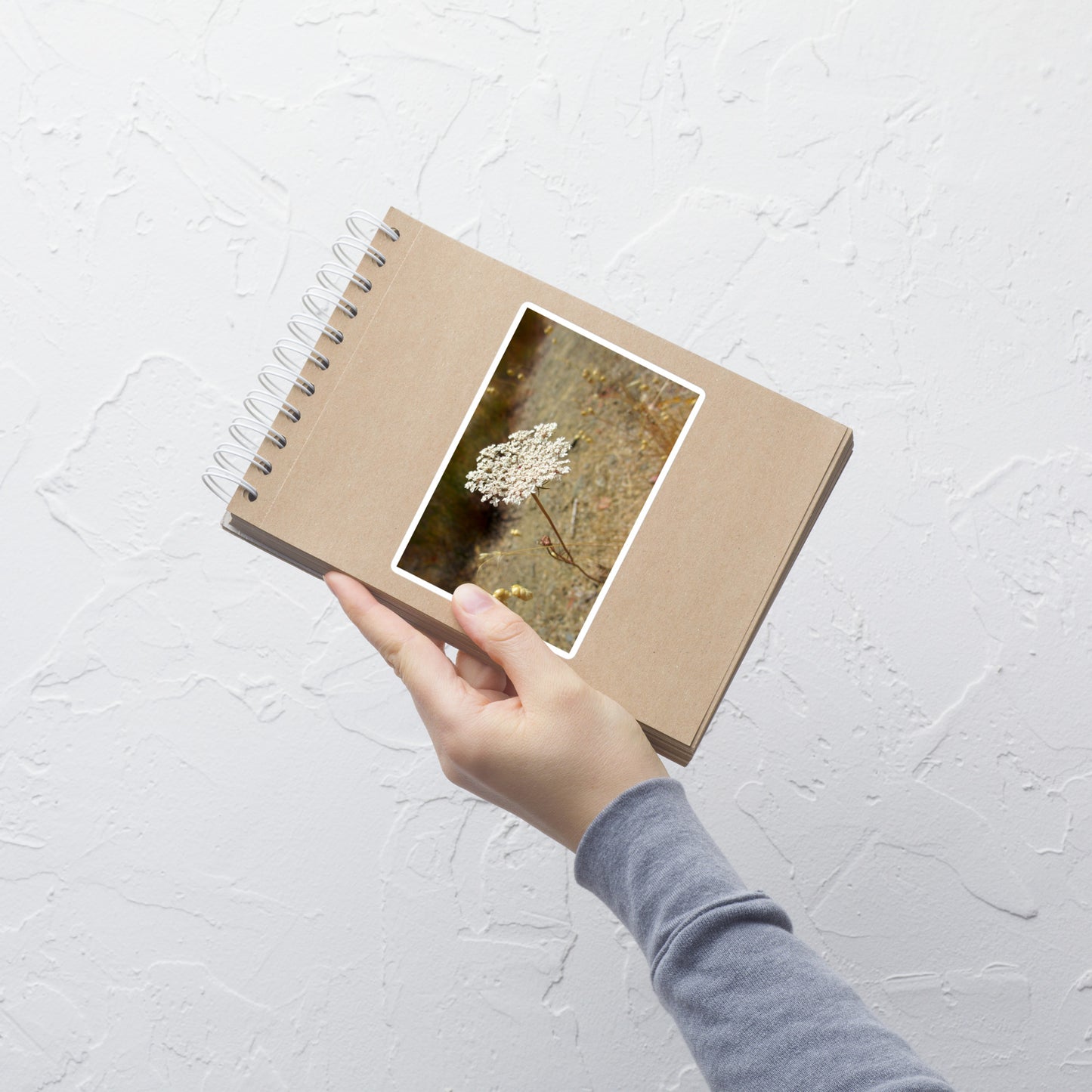 Lifestyle photo of a rectangular vinyl sticker with an image of a white Queen Anne's Lace bloom, placed on a small notepad.
