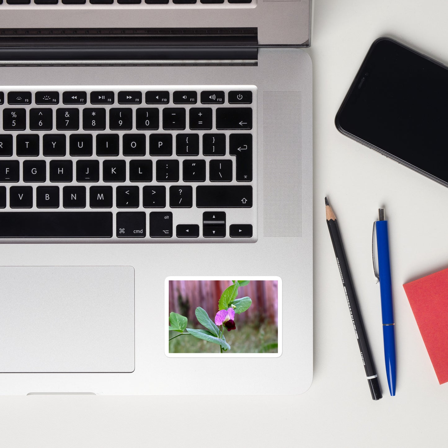 Lifestyle photo of a rectangular vinyl sticker with an image of a sweet pea bloom, placed on a laptop to the right of the mouse pad.