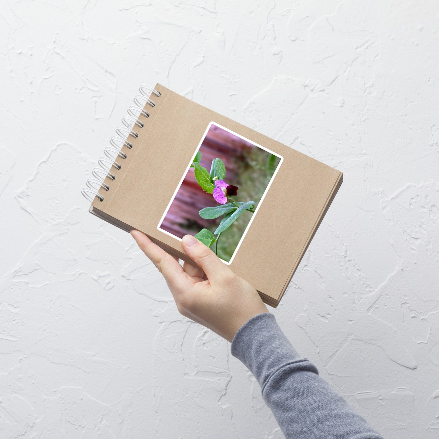 Lifestyle photo of a rectangular vinyl sticker with an image of a sweet pea bloom, placed on a small notepad.