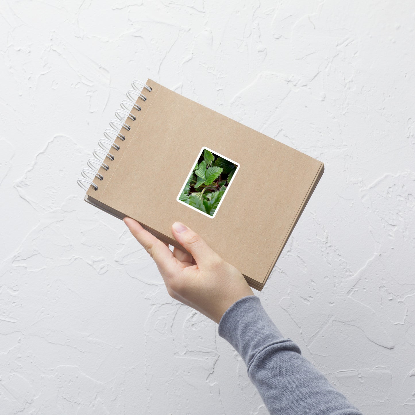 Lifestyle photo of a rectangular vinyl sticker with a close-up image of strawberry leaves, placed on a small notepad.