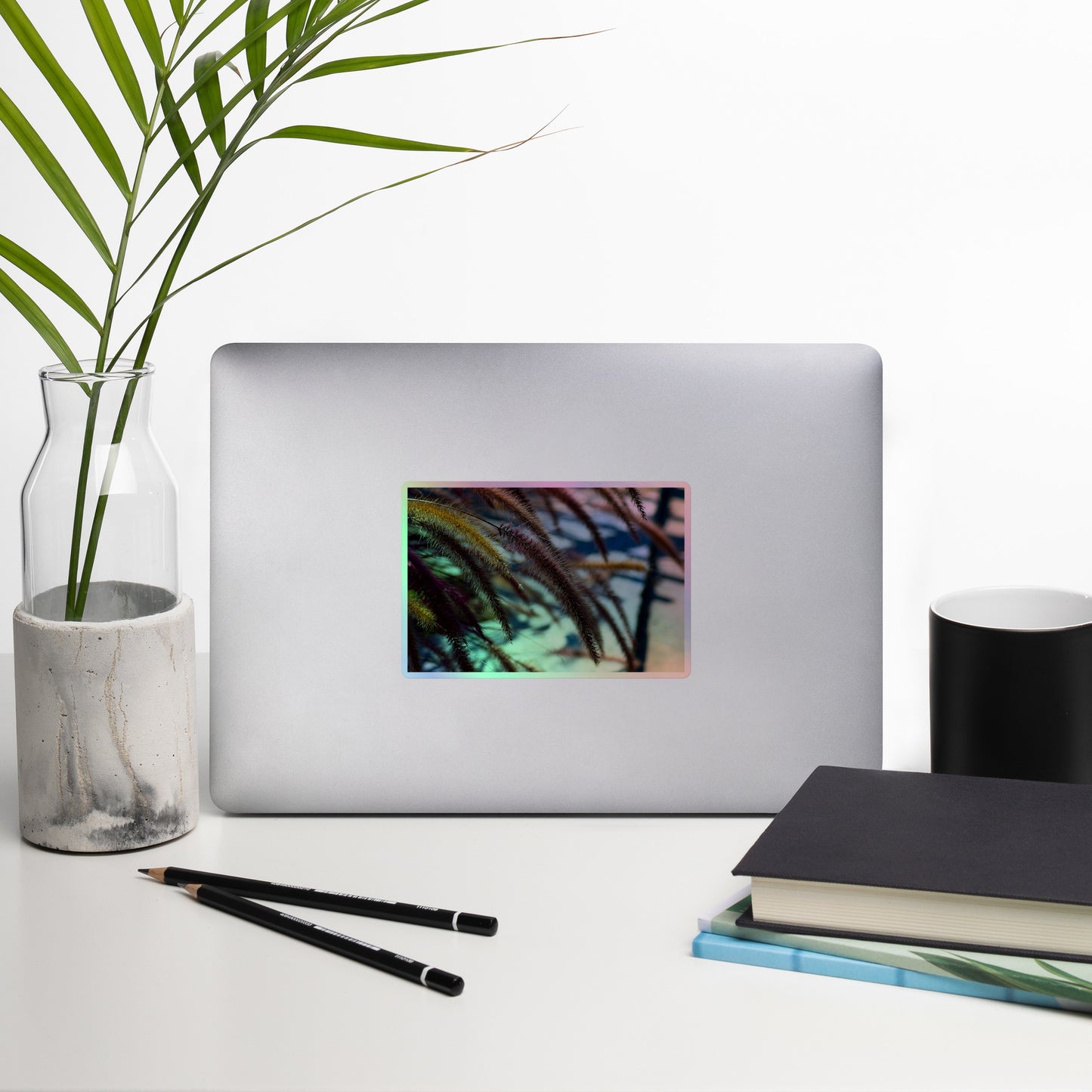 Lifestyle photo of a rectangular holographic sticker with an image ofgolden purple foxtails breeze, placed on a laptop with desk supplies nearby.