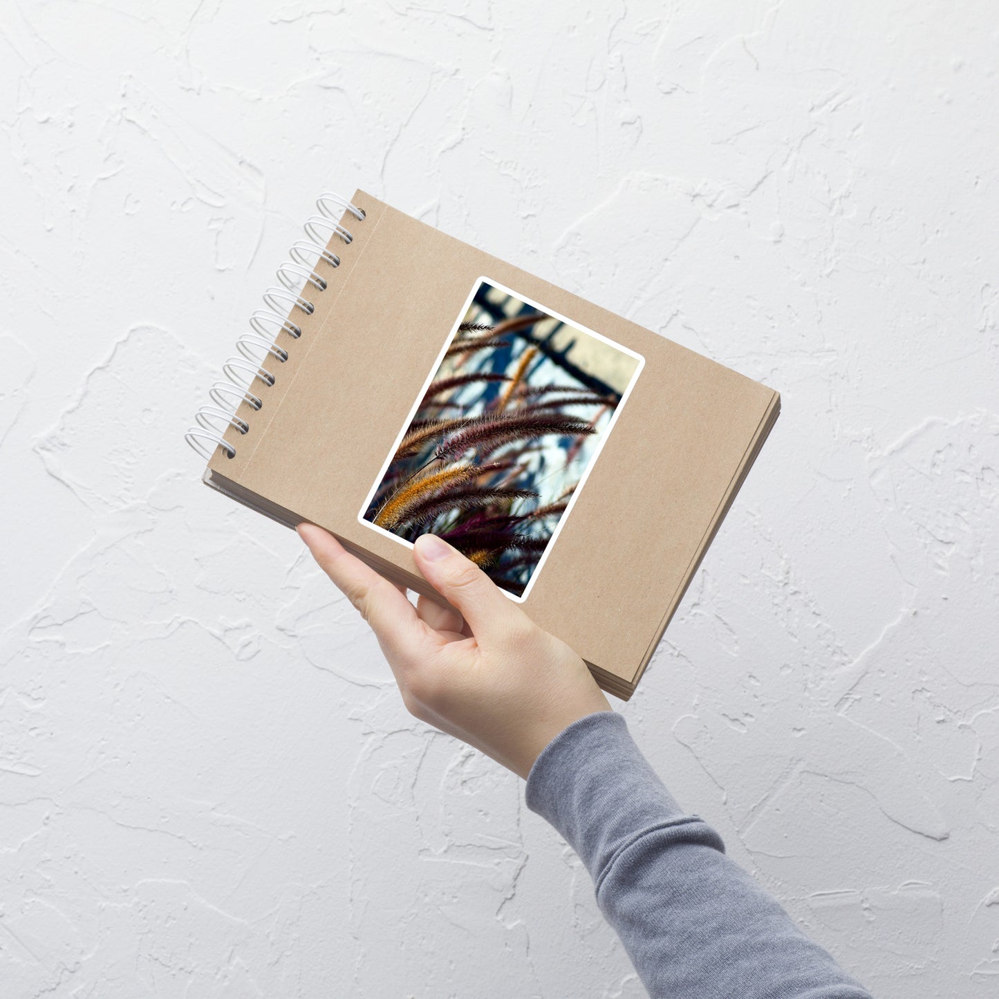Lifestyle photo of a rectangular vinyl sticker with an image of yellow and purple foxtails, placed on a small notepad.