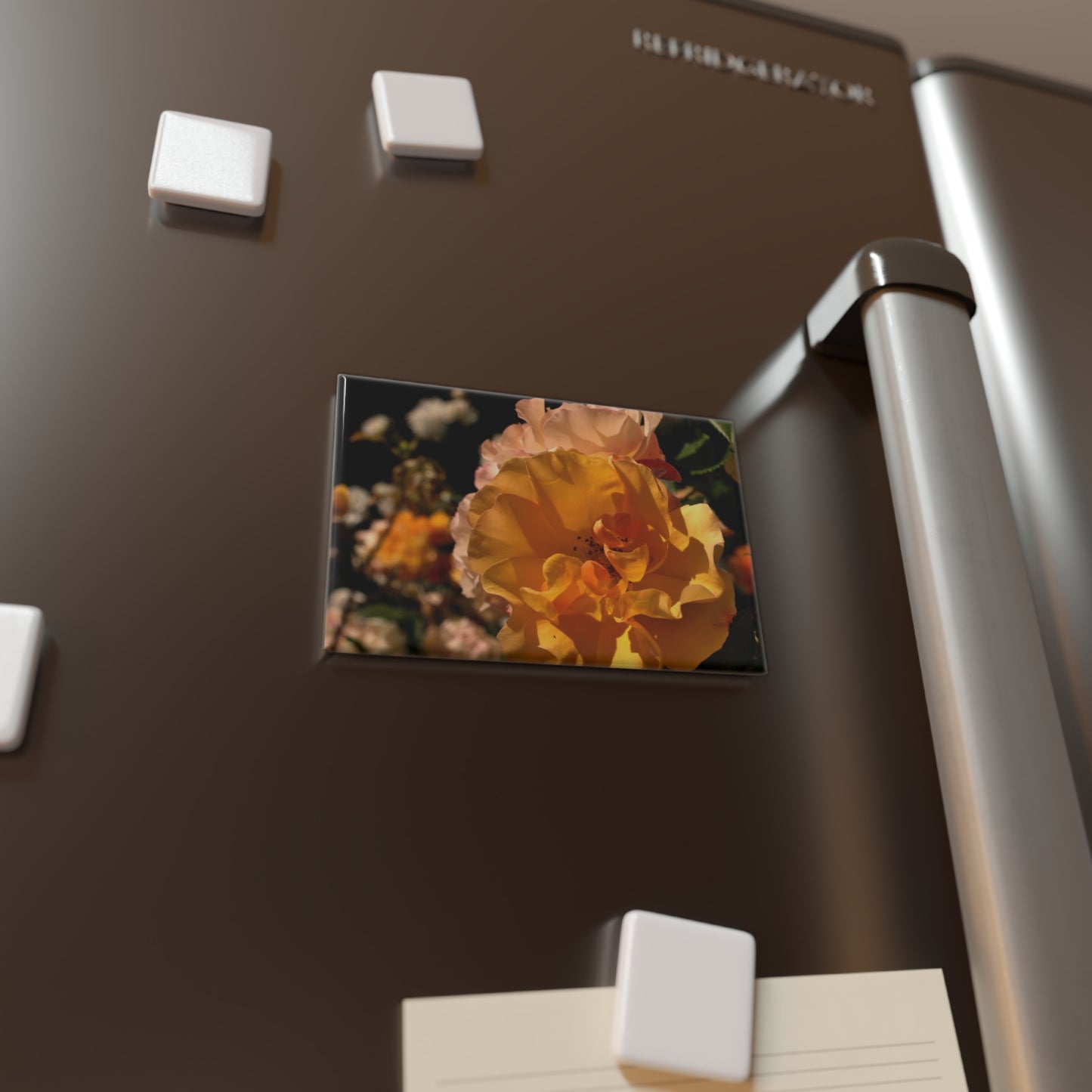 Lifestyle photo of a rectangular button magnet with an image of a golden yellow and pastel pink rose cluster, placed on a fridge.