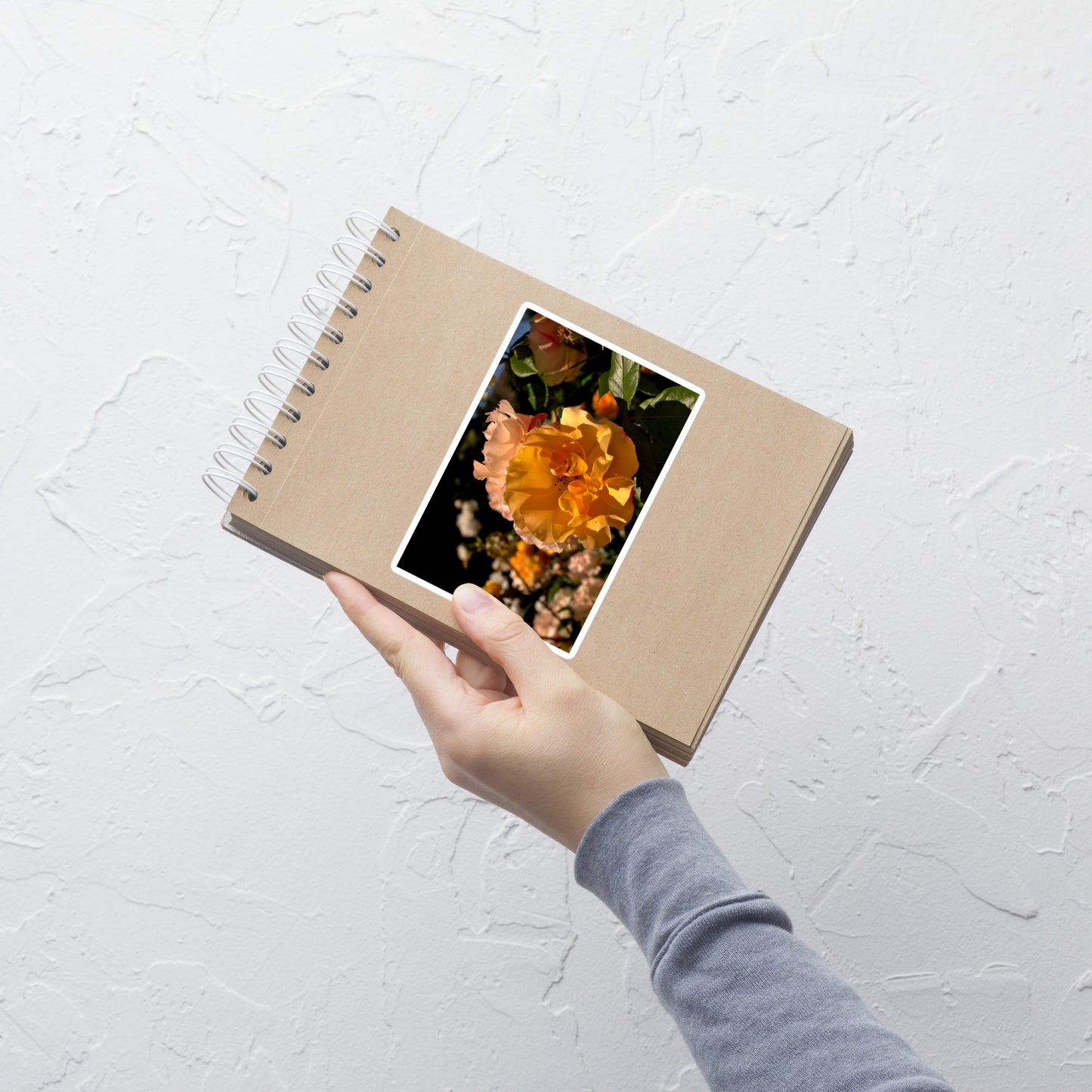 Lifestyle photo of a rectangular vinyl sticker with an image of pastel pink and yellow roses in garden, placed on a small notepad.