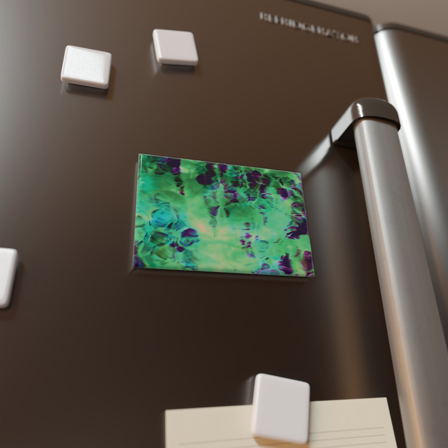 Lifestyle photo of a rectangular button magnet with an image of a vivid green and purple water reflection design, placed on a fridge.
