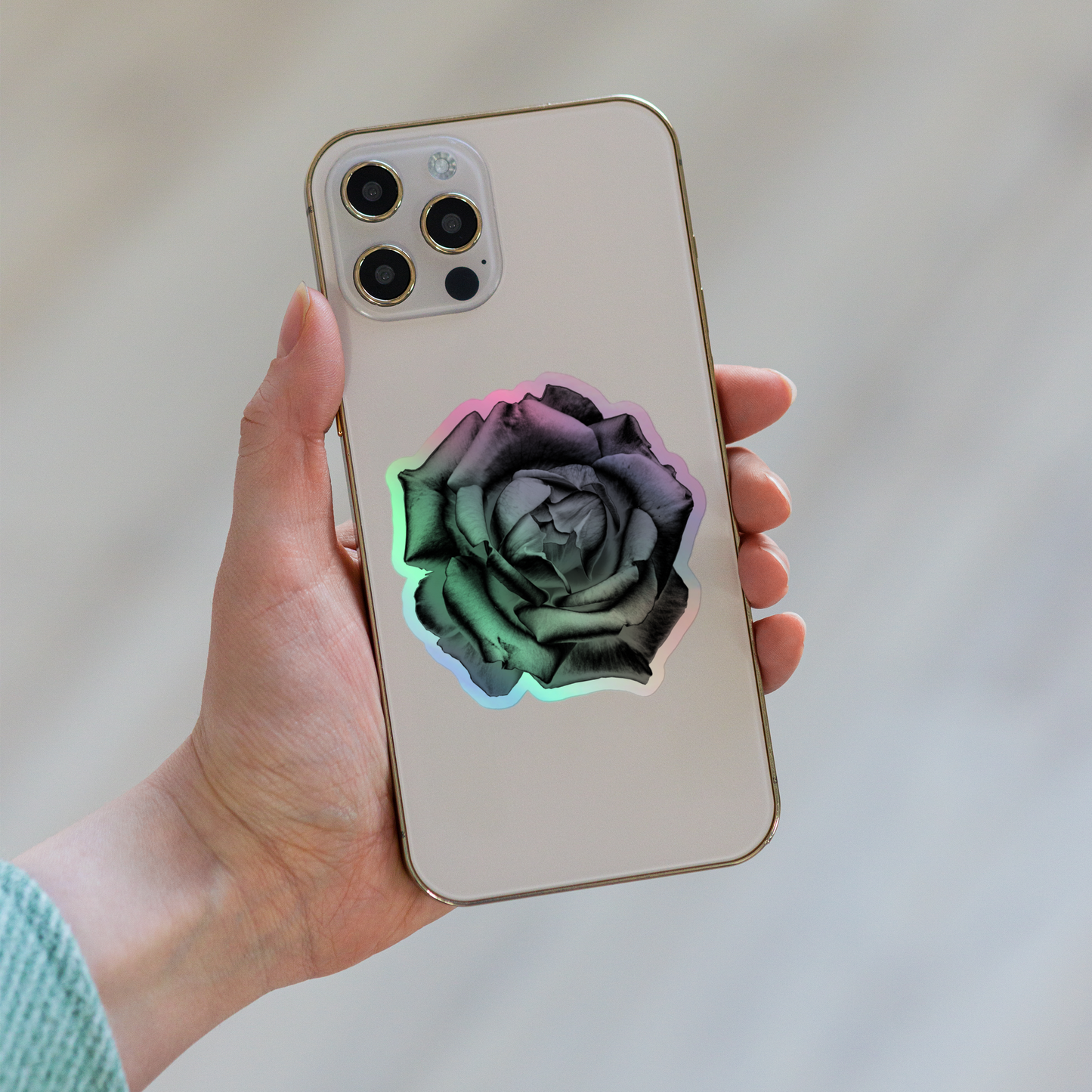 Lifestyle photo of a kiss-cut holographic sticker with an image of a grey charcoal drawing style rose design, placed on the back of a phone.