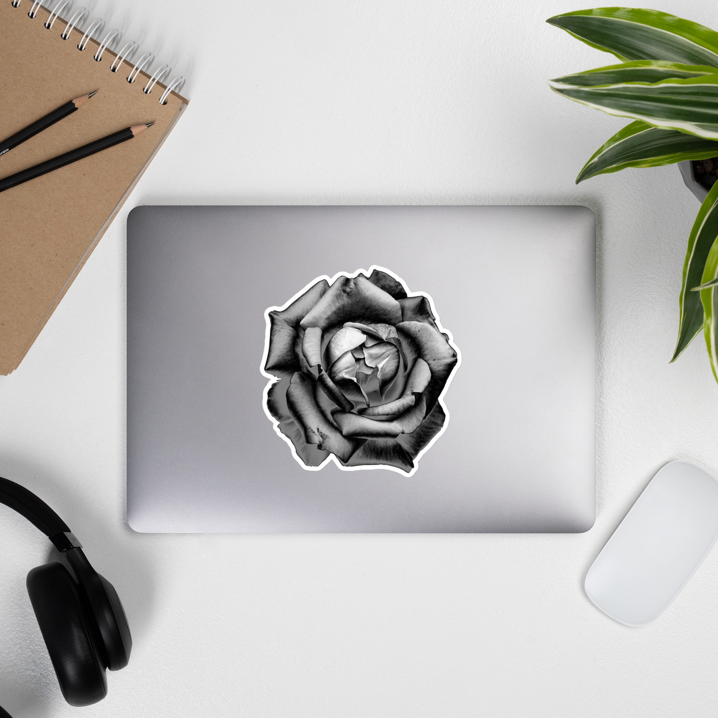 Lifestyle photo of a kiss-cut vinyl sticker with an image of a grey charcoal drawing style rose, placed on the outside of a laptop.