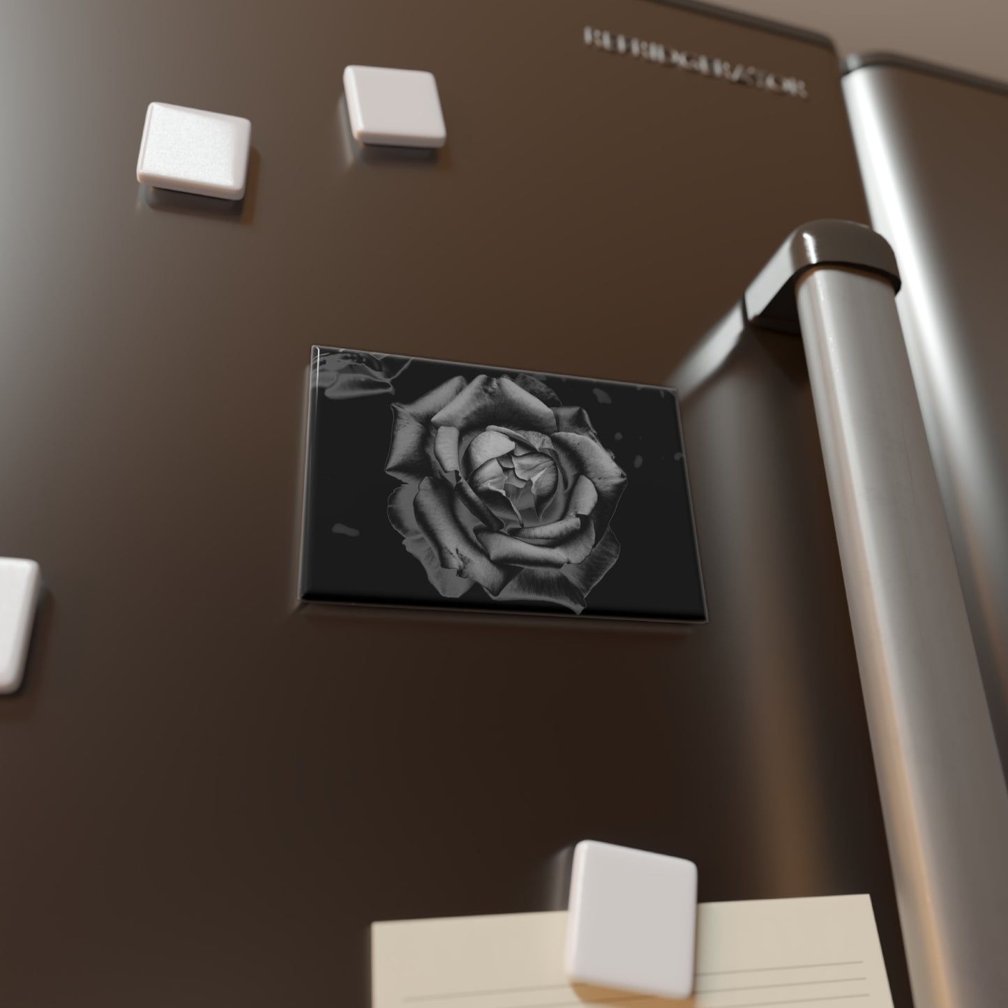 Lifestyle photo of a rectangular button magnet with an image of a charcoal drawing rose design, placed on a fridge.