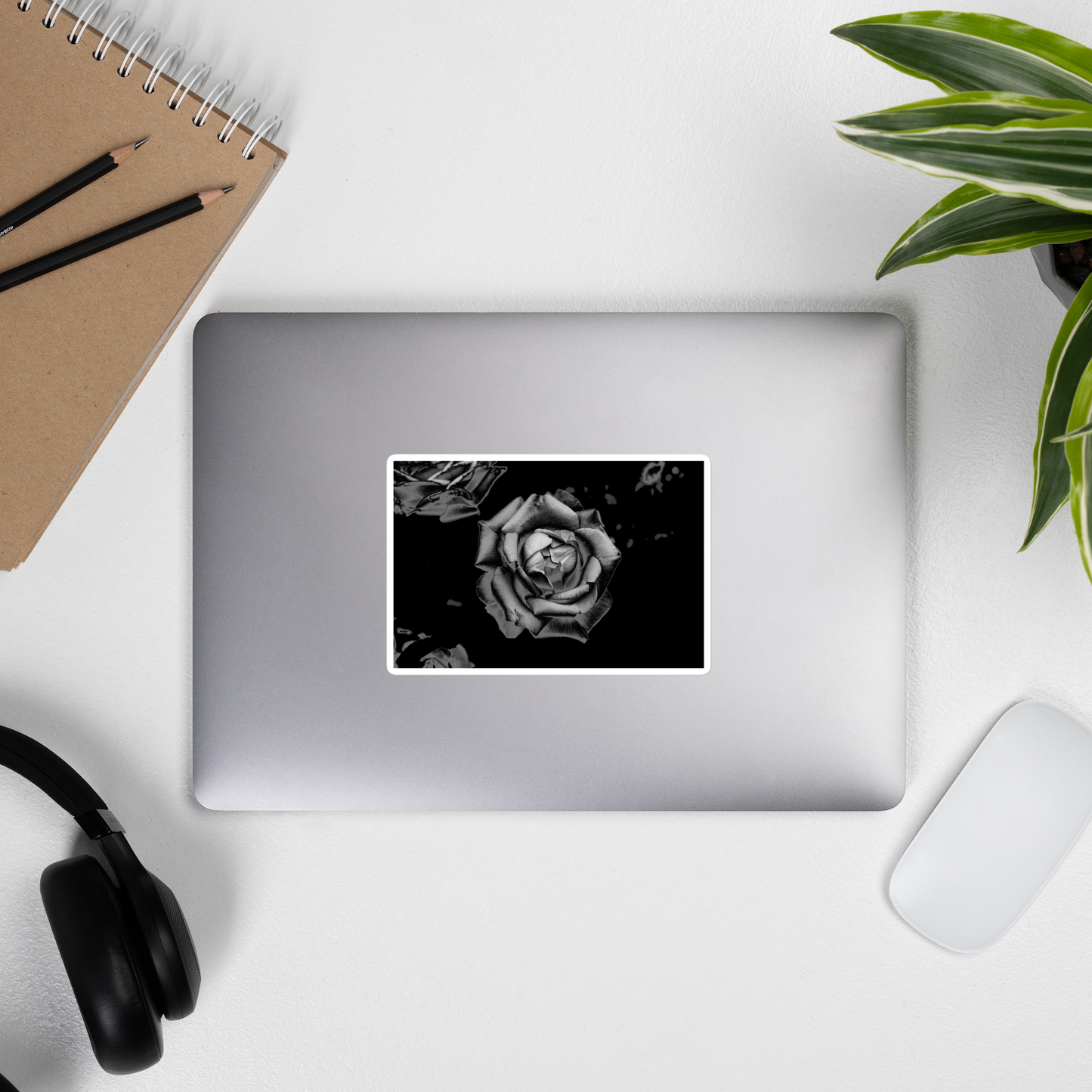 Lifestyle photo of a rectangular vinyl sticker with an image of a grey charcoal rose design, placed on the outside of a laptop.