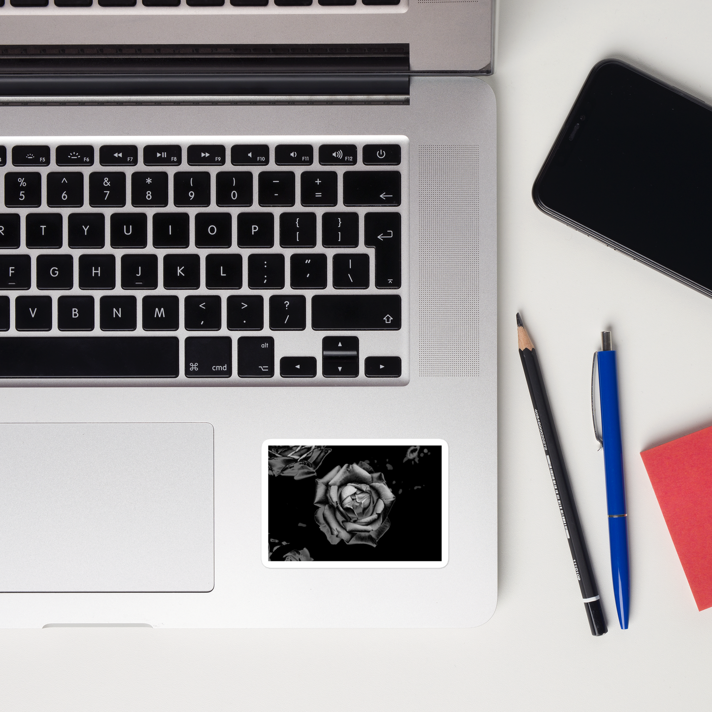 Lifestyle photo of a rectangular vinyl sticker with an image of a grey charcoal rose design, placed on a laptop to the right of the mouse pad.