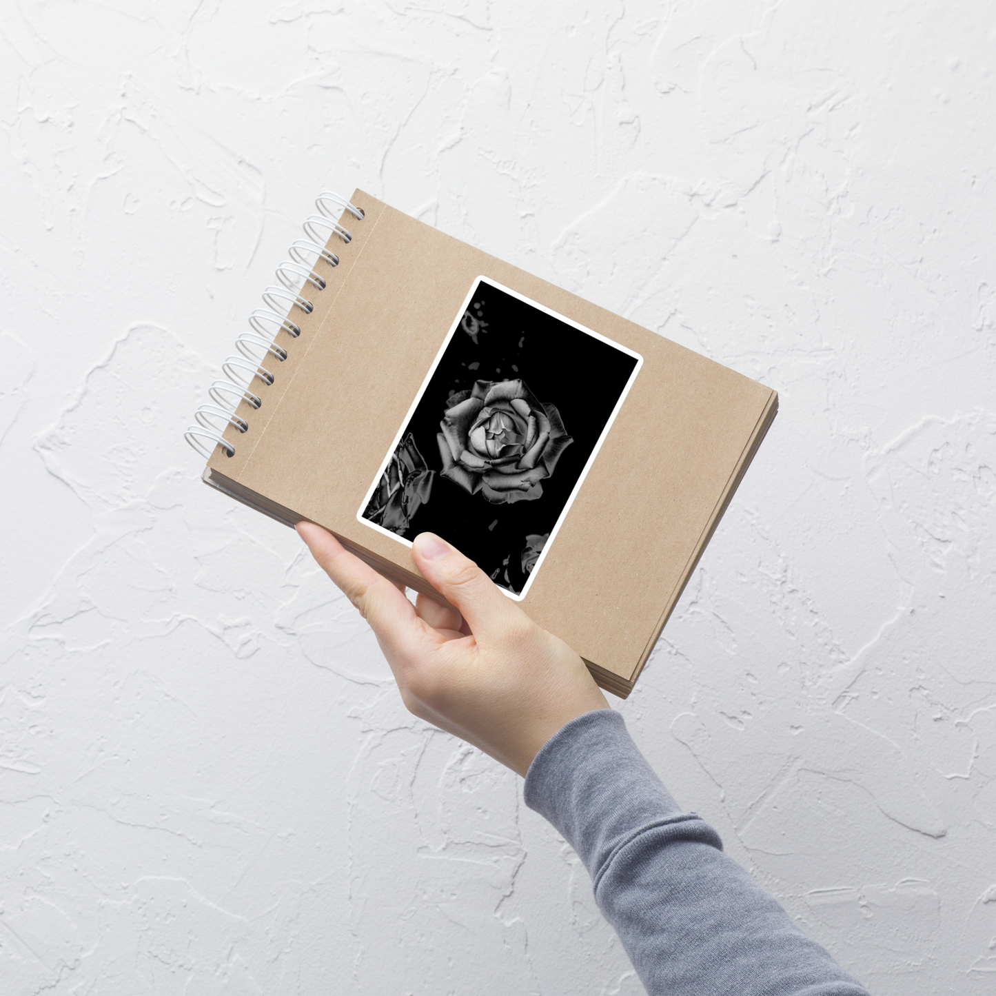 Lifestyle photo of a rectangular vinyl sticker with an image of a grey charcoal rose design, placed on a small notepad.