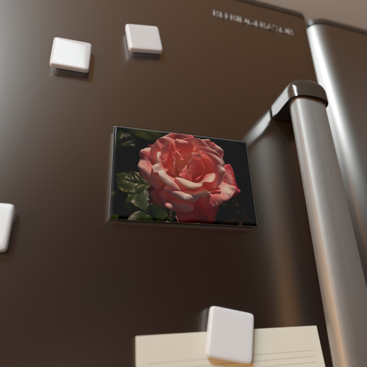 Lifestyle photo of a rectangular button magnet with an image of a high contrast pink rose with deep green leaves, placed on a fridge.