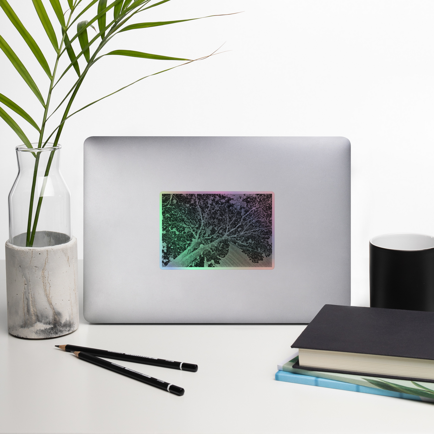 Lifestyle photo of a rectangular holographic sticker with an image of a light embossed tree lightning design, placed on a laptop with desk supplies nearby.