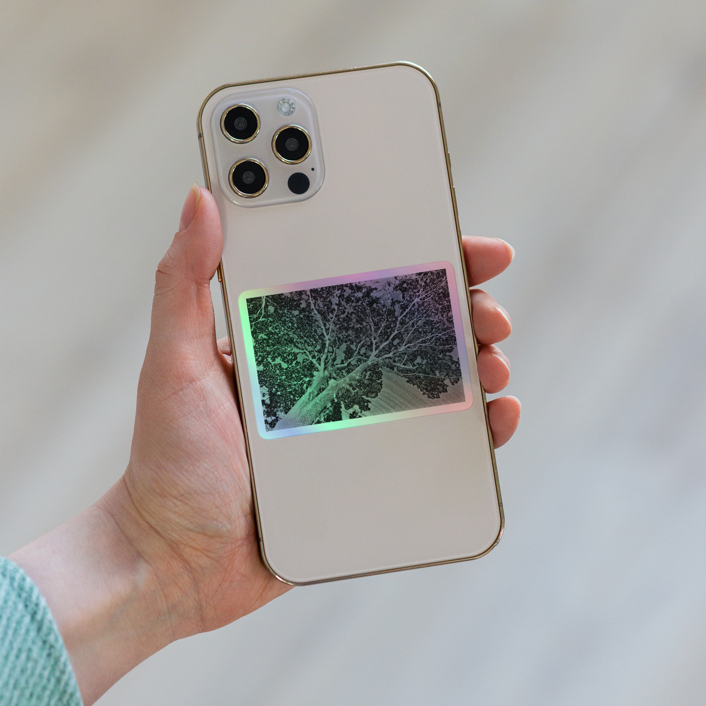 Lifestyle photo of a rectangular holographic sticker with an image of a light embossed tree lightning design, placed on the back of a phone.