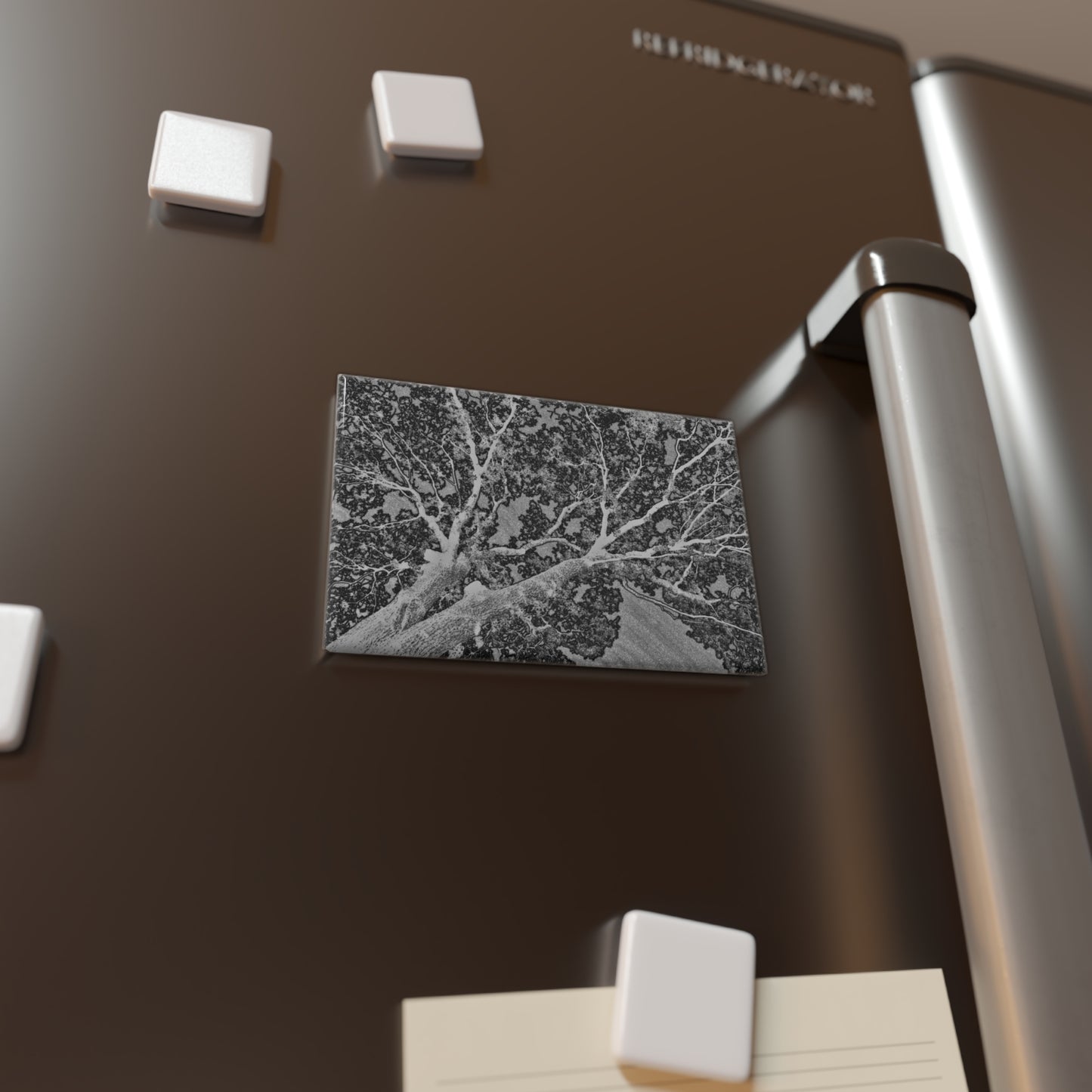 Lifestyle photo of a rectangular button magnet with an image of an embossed tree design with lightning like features, placed on a fridge.
