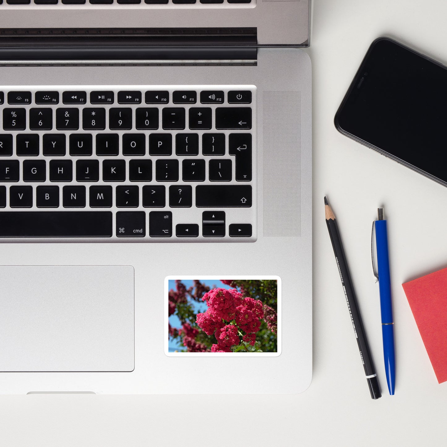 Lifestyle photo of a rectangular vinyl sticker with an image of vivid pink crape myrtle blooms, placed on a laptop to the right of the mouse pad.