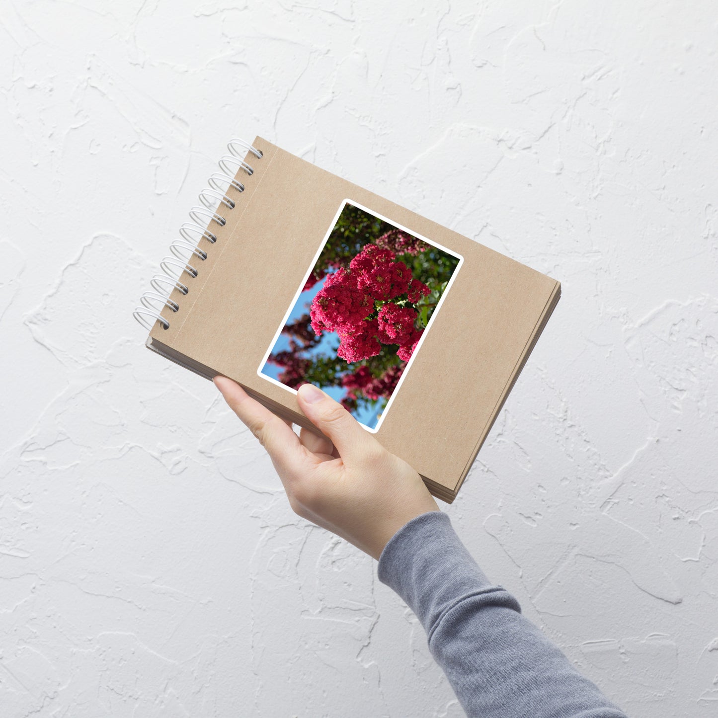 Lifestyle photo of a rectangular vinyl sticker with an image of vivid pink crape myrtle blooms, placed on a small notepad.